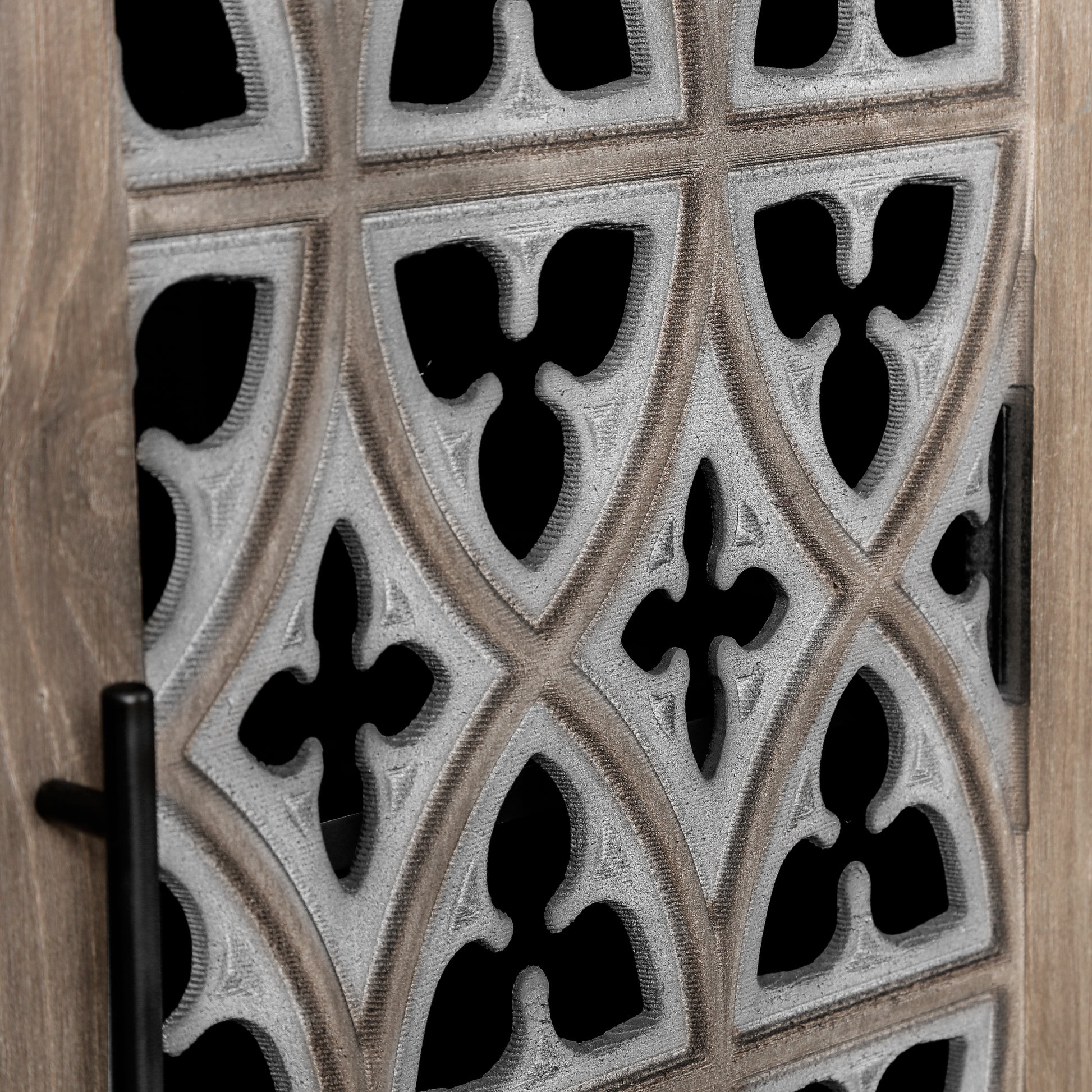 Closeup of antique wood cabinet door with decorative gothic fretwork detail and black handle