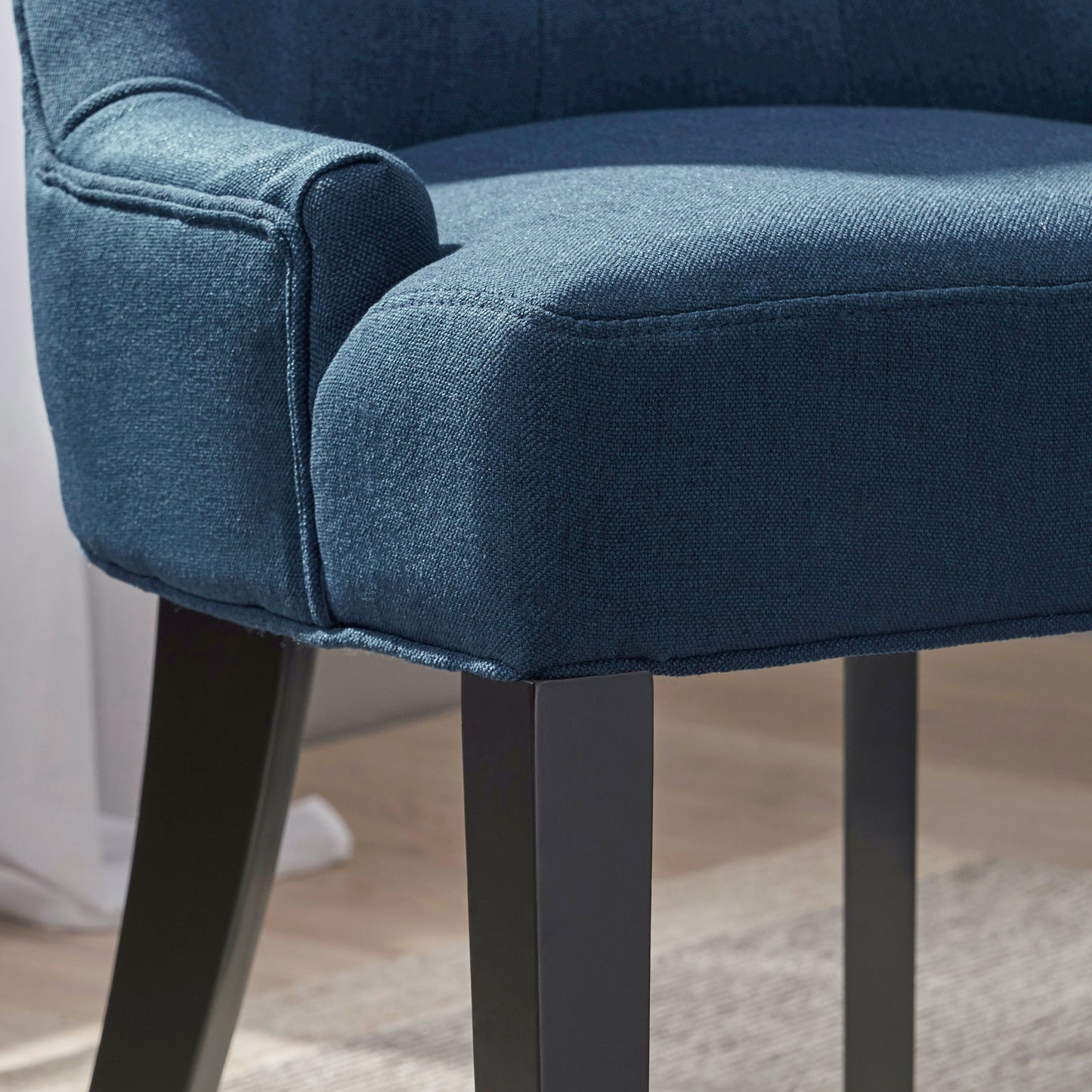Closeup of a navy blue upholstered armchair armrest with detailed stitching