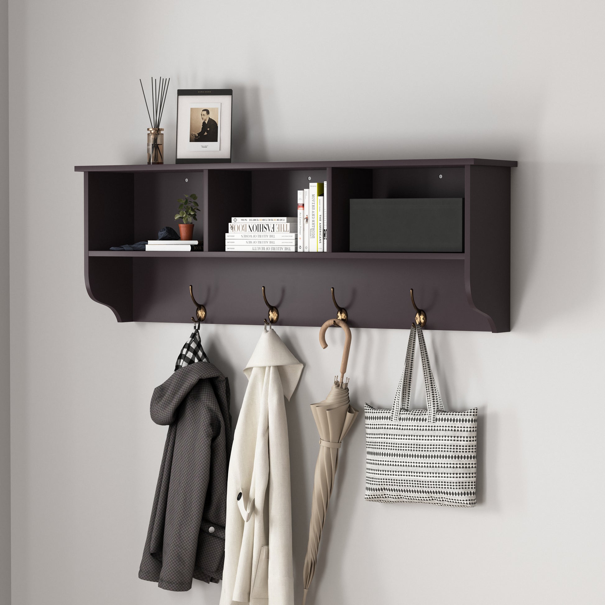 Dark wood entryway shelf with brass hooks holding coats umbrella and tote bag