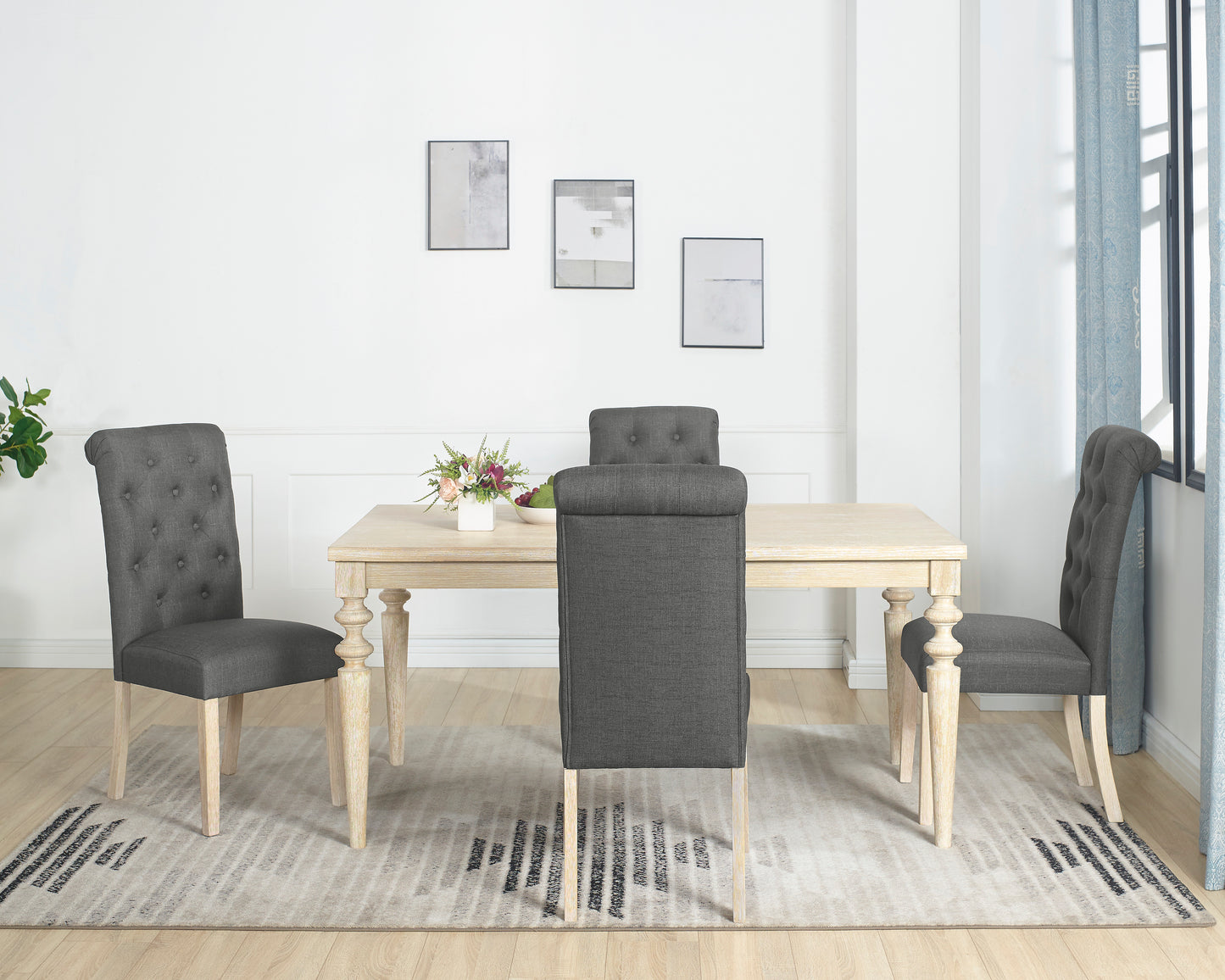 Dark grey tufted dining chairs with carved wood legs surrounding a light wood table