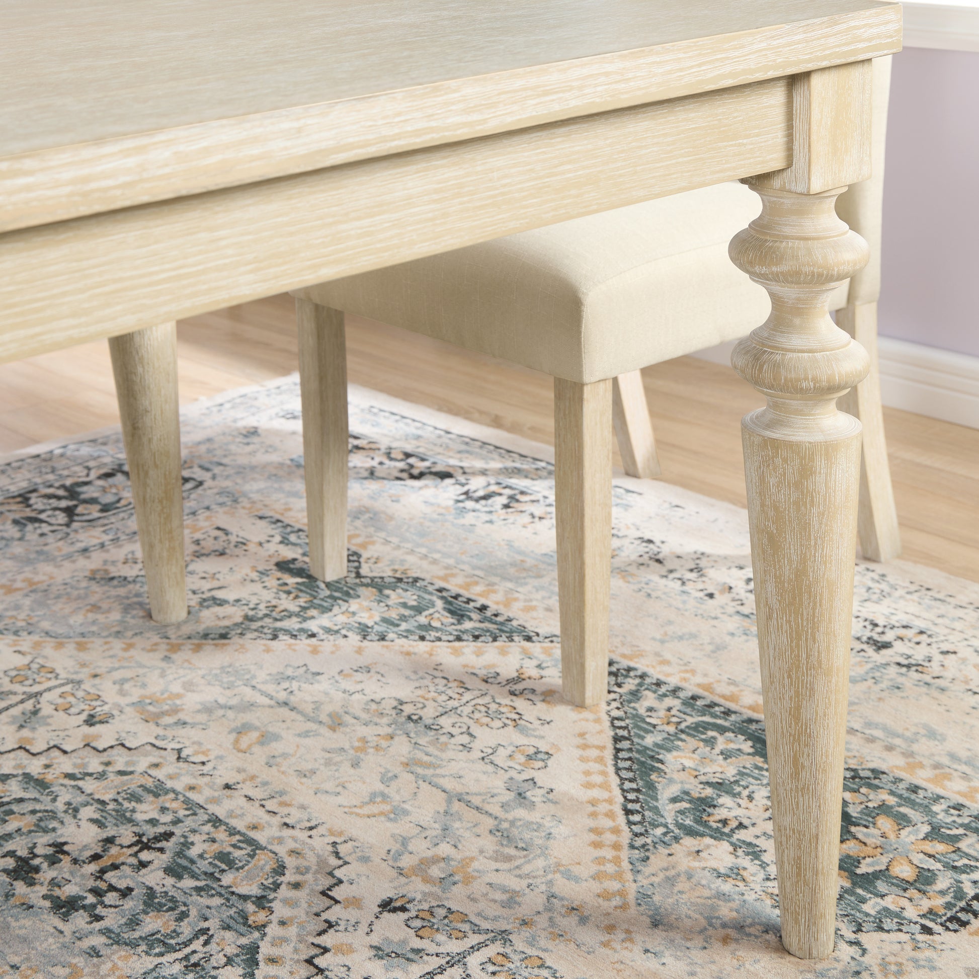 Light oak dining table leg with turned detail on ornate rug