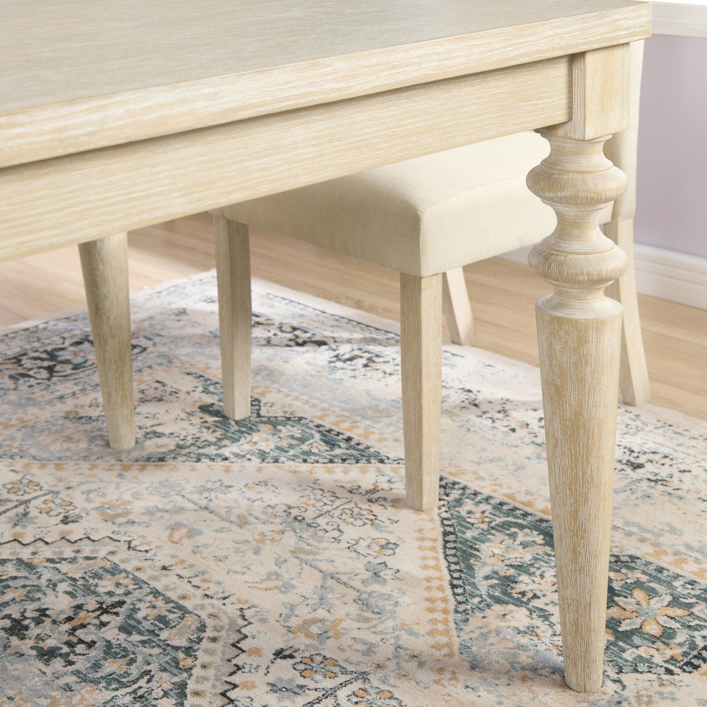Cream distressed wood dining table leg with turned detail on ornate rug