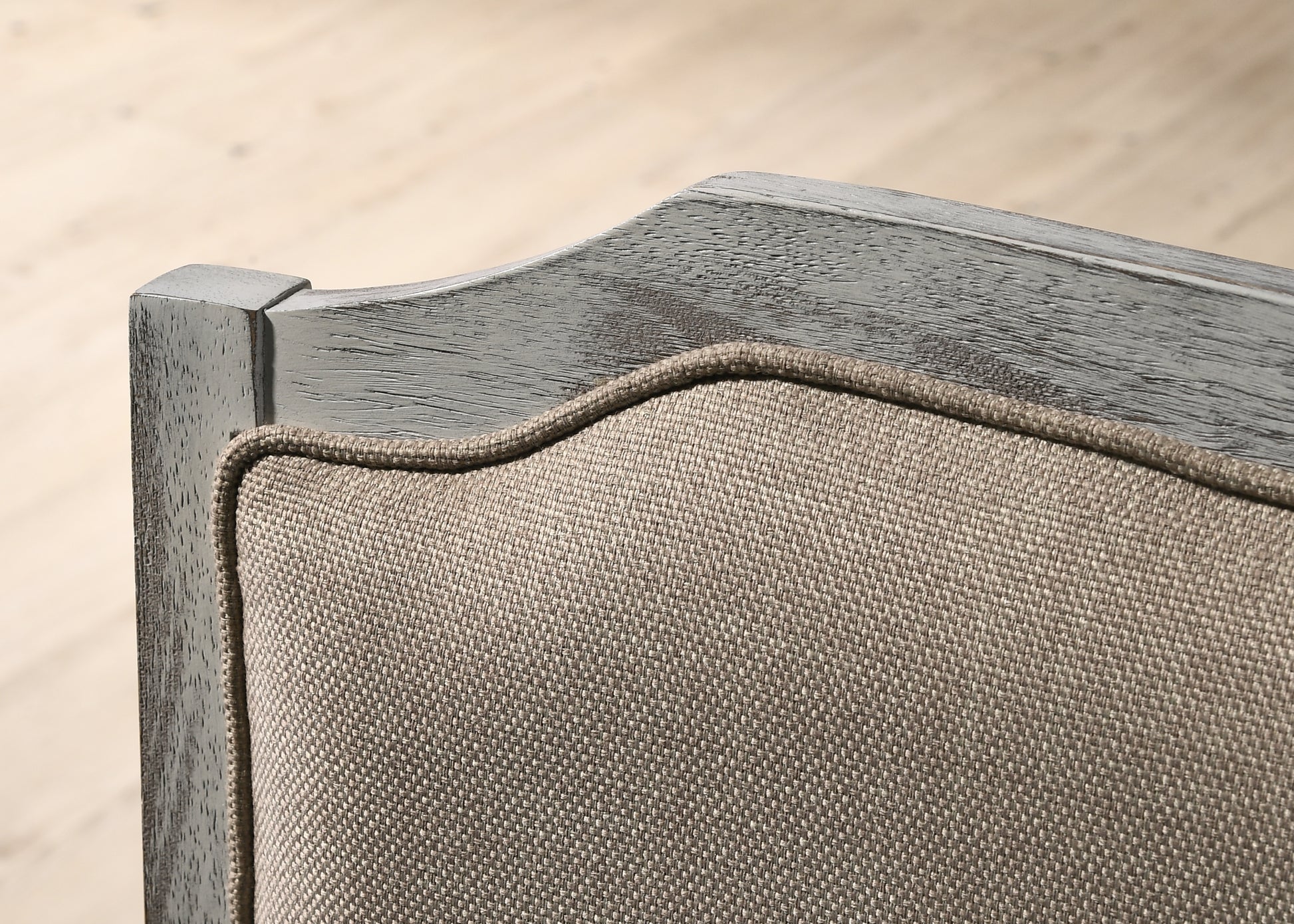 Closeup of a gray distressed wood frame accentuating the beige linen upholstery of a decorative chair