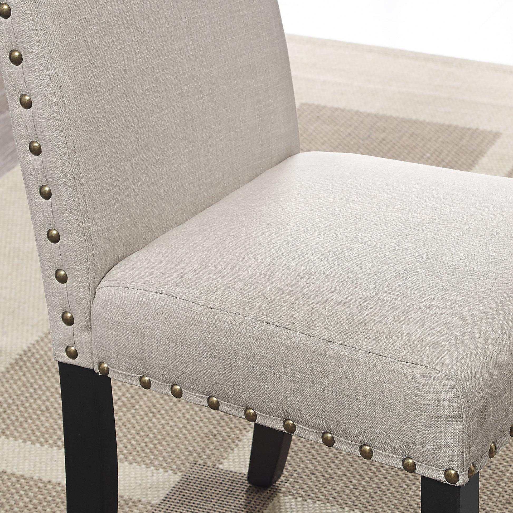 Closeup of a light beige upholstered dining chair with brass nailhead trim and black legs