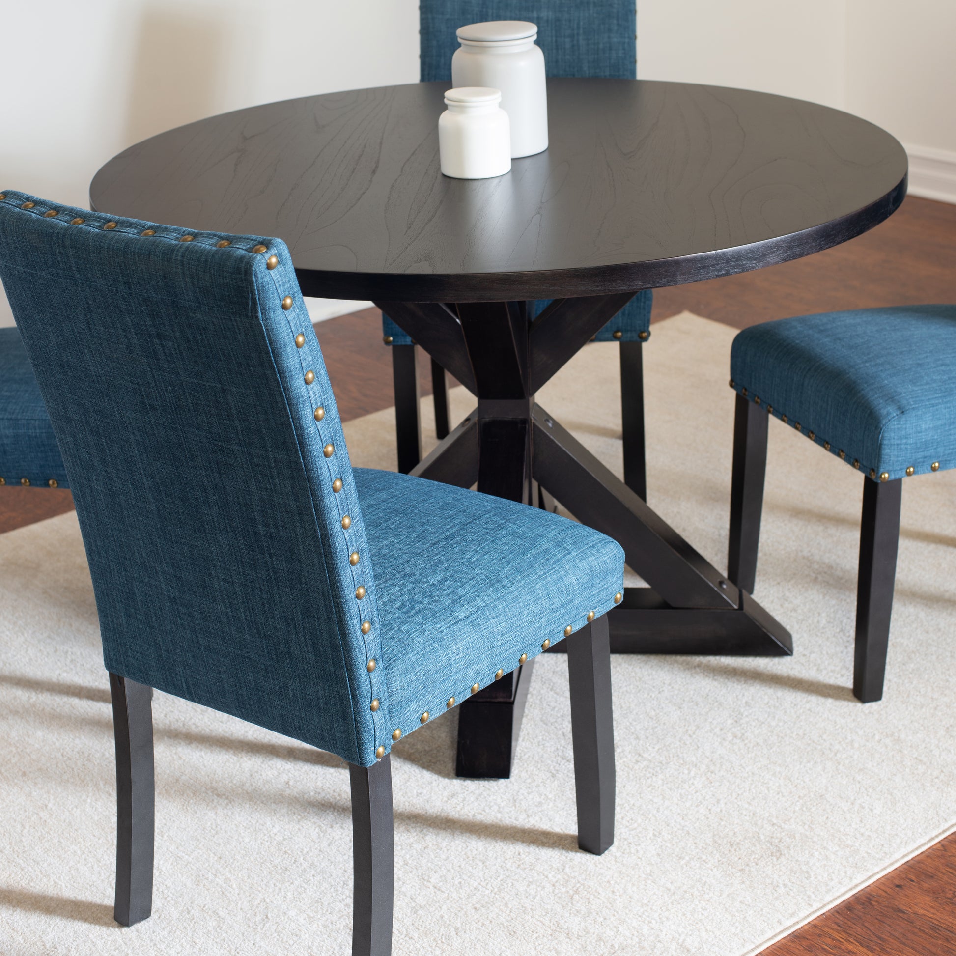 Dark wood round dining table with teal upholstered chairs featuring brass nailhead trim