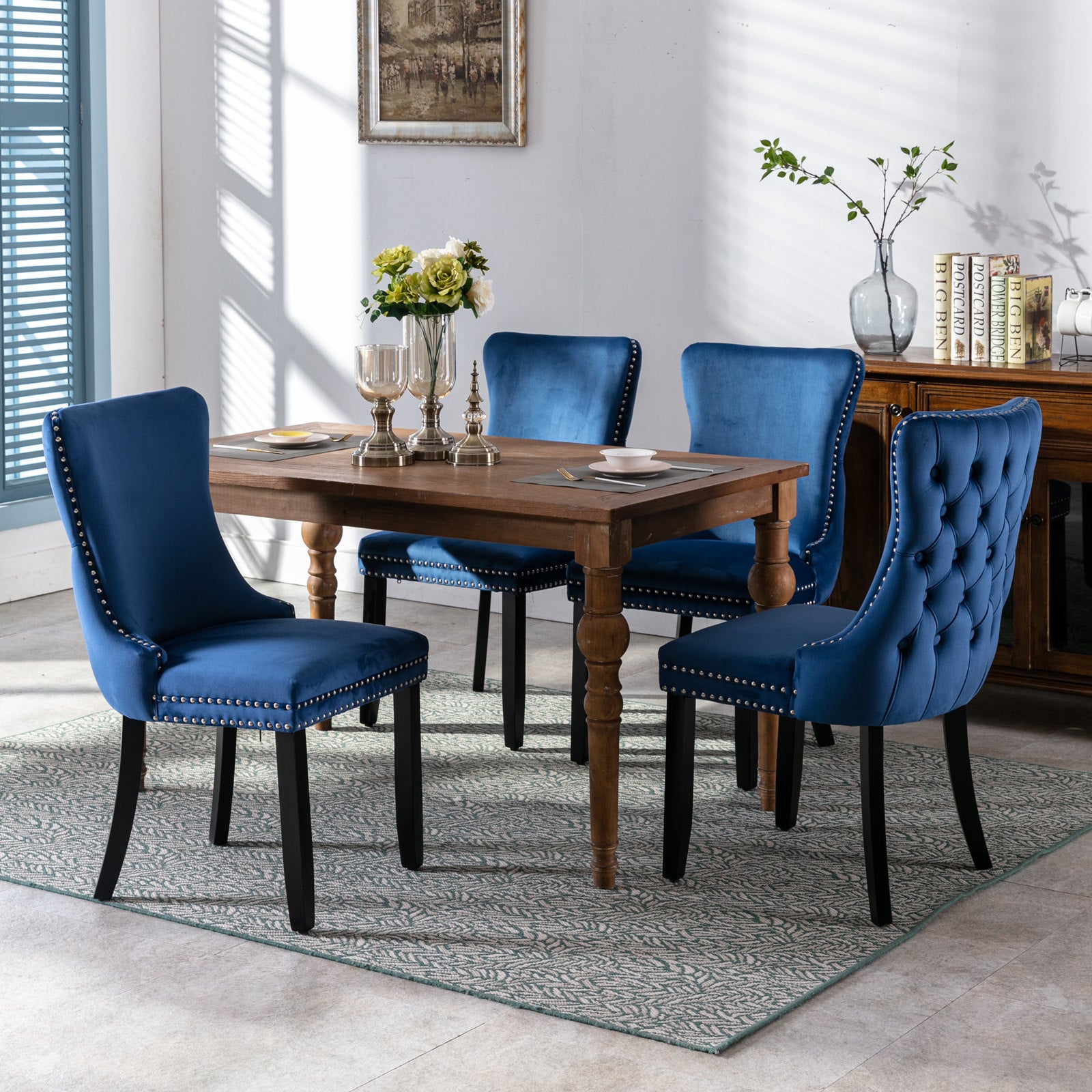 Four navy blue velvet dining chairs with silver stud accents around a wooden table