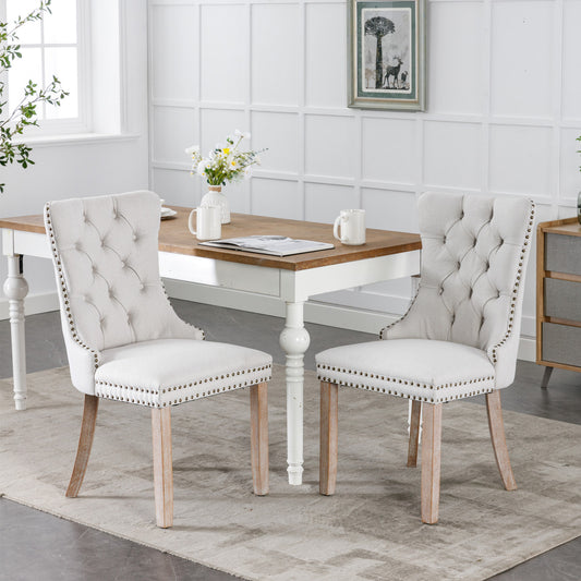 Two tufted cream upholstered dining chairs with nailhead trim and natural wood legs