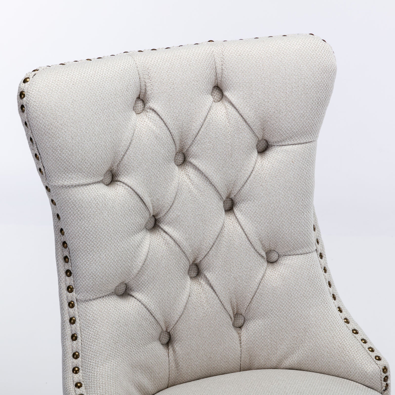 Closeup of a beige tufted upholstered armchair back with brass nailhead trim