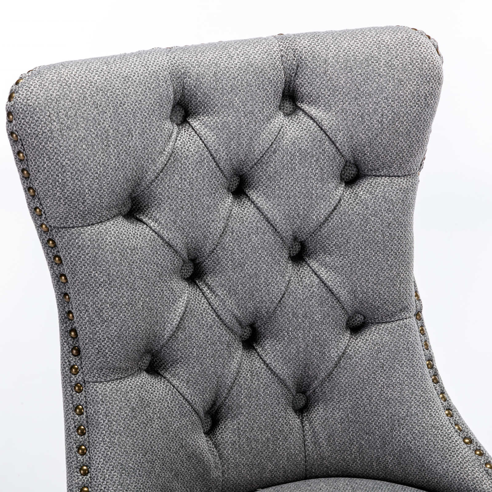 Closeup of tufted grey fabric dining chair back with brass nailhead trim