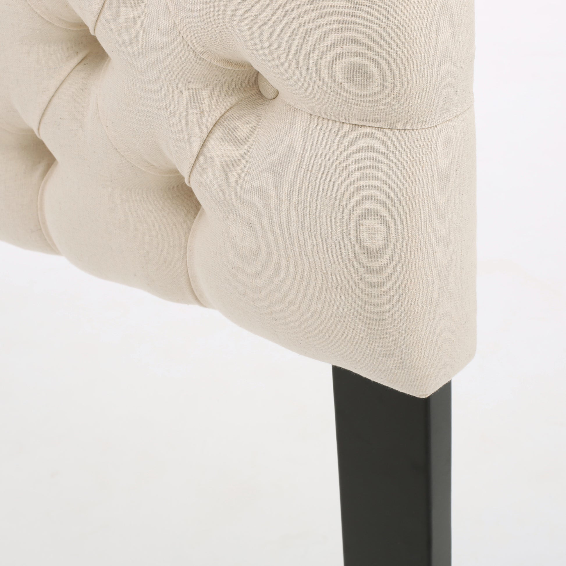 Cream linen tufted headboard detail with a dark metal leg