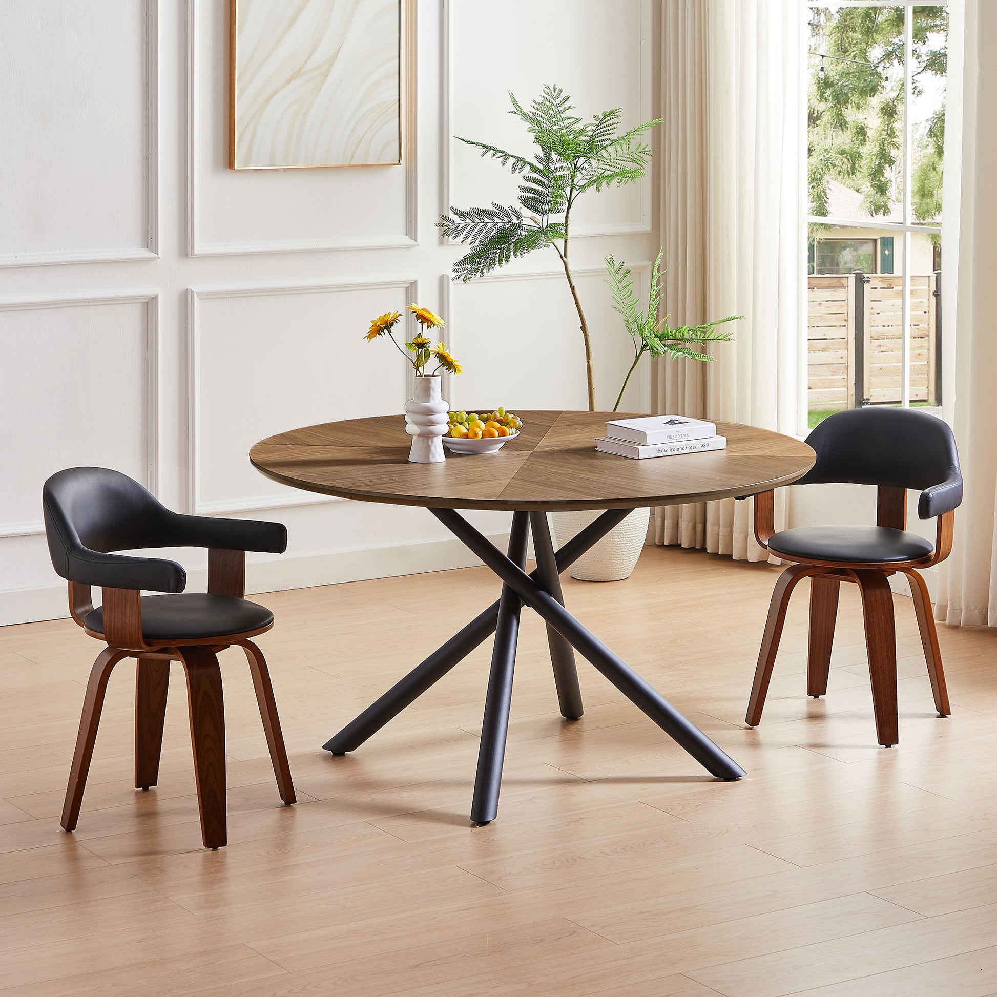 Round walnut dining table with black metal base and two black leather chairs