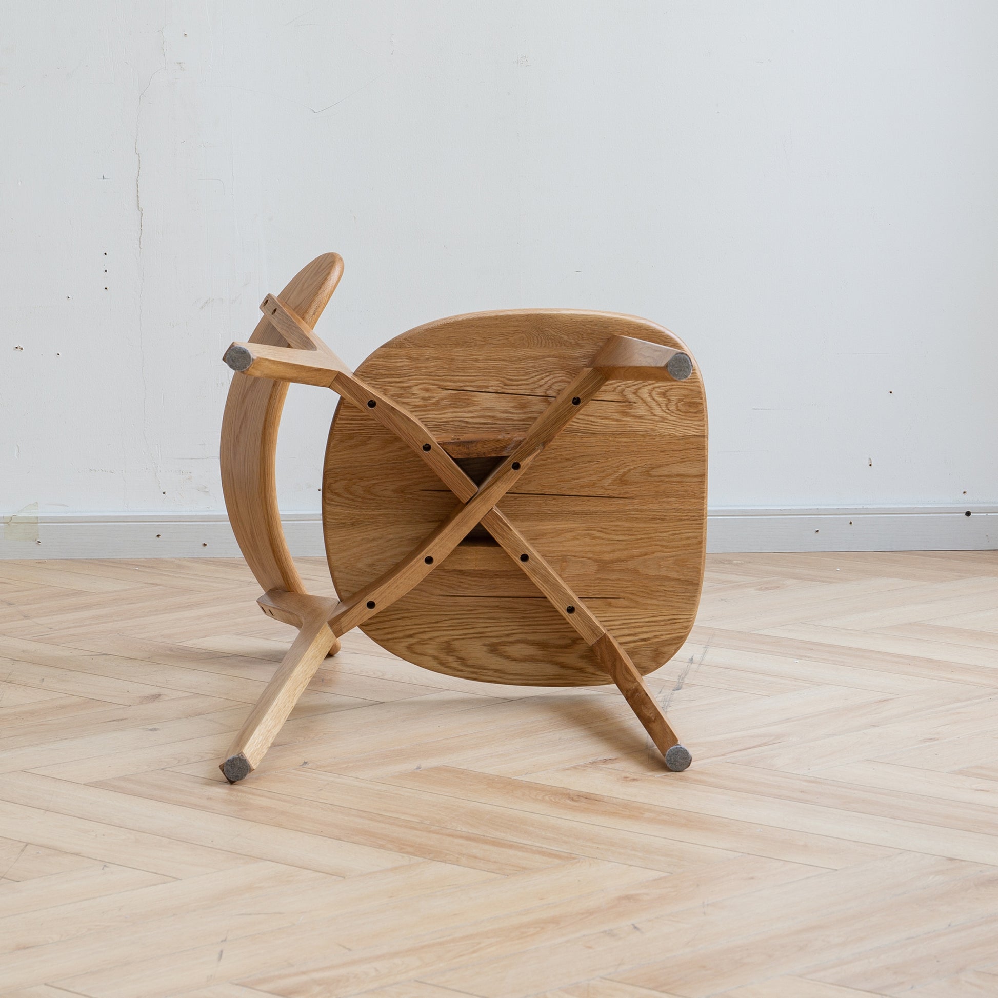 Natural oak dining chair with curved back upside down on a wooden floor
