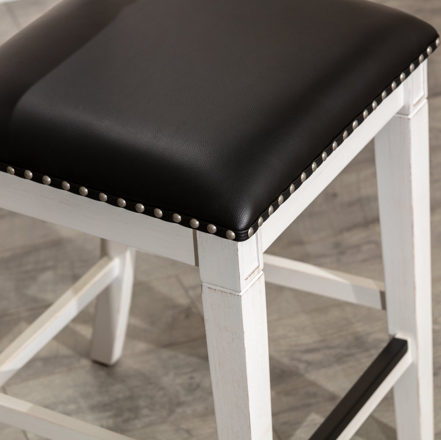 Black faux leather counter stool with distressed white wooden frame and silver nailhead trim