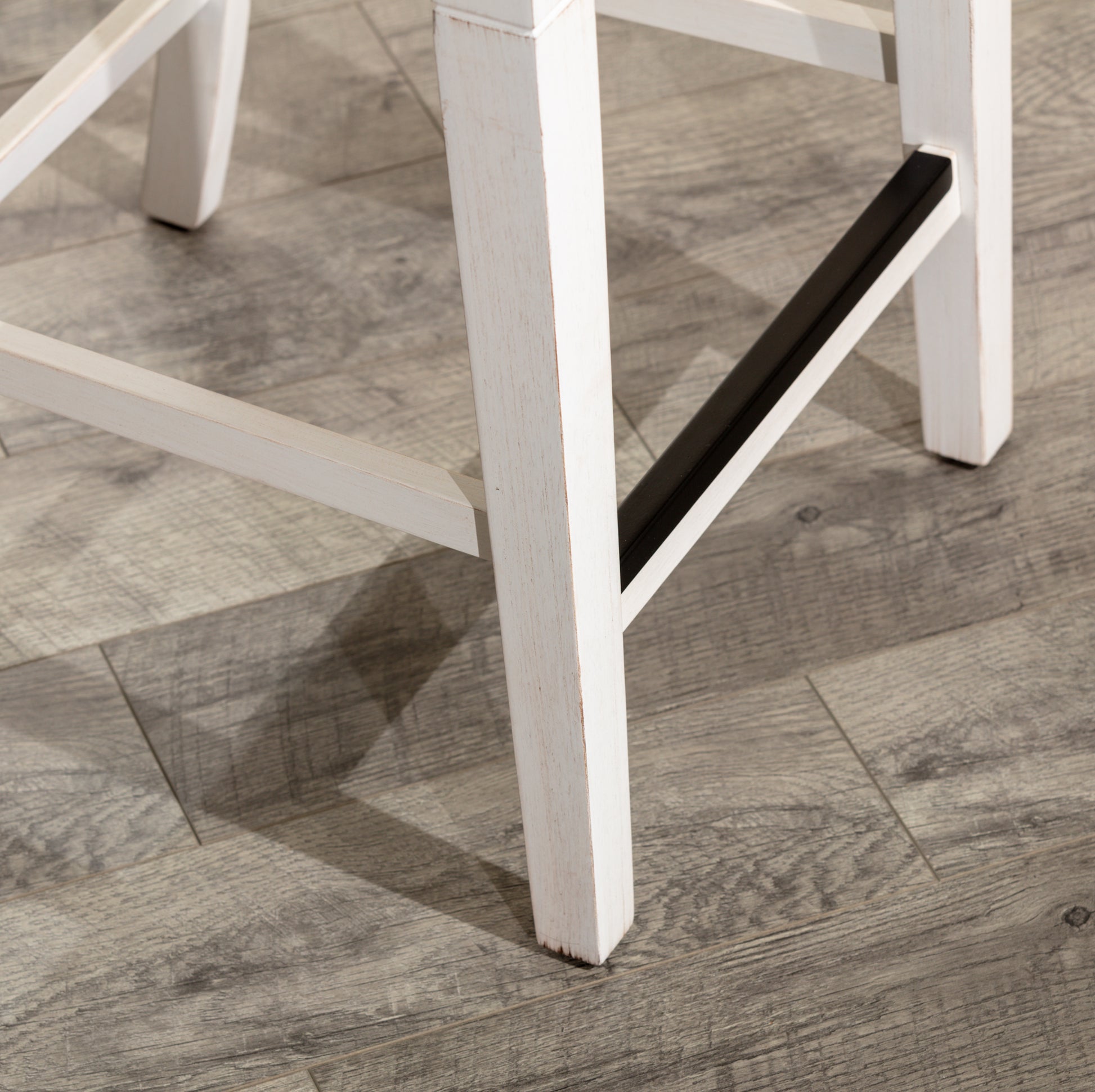 White distressed wood bar stool leg detail with black footrest
