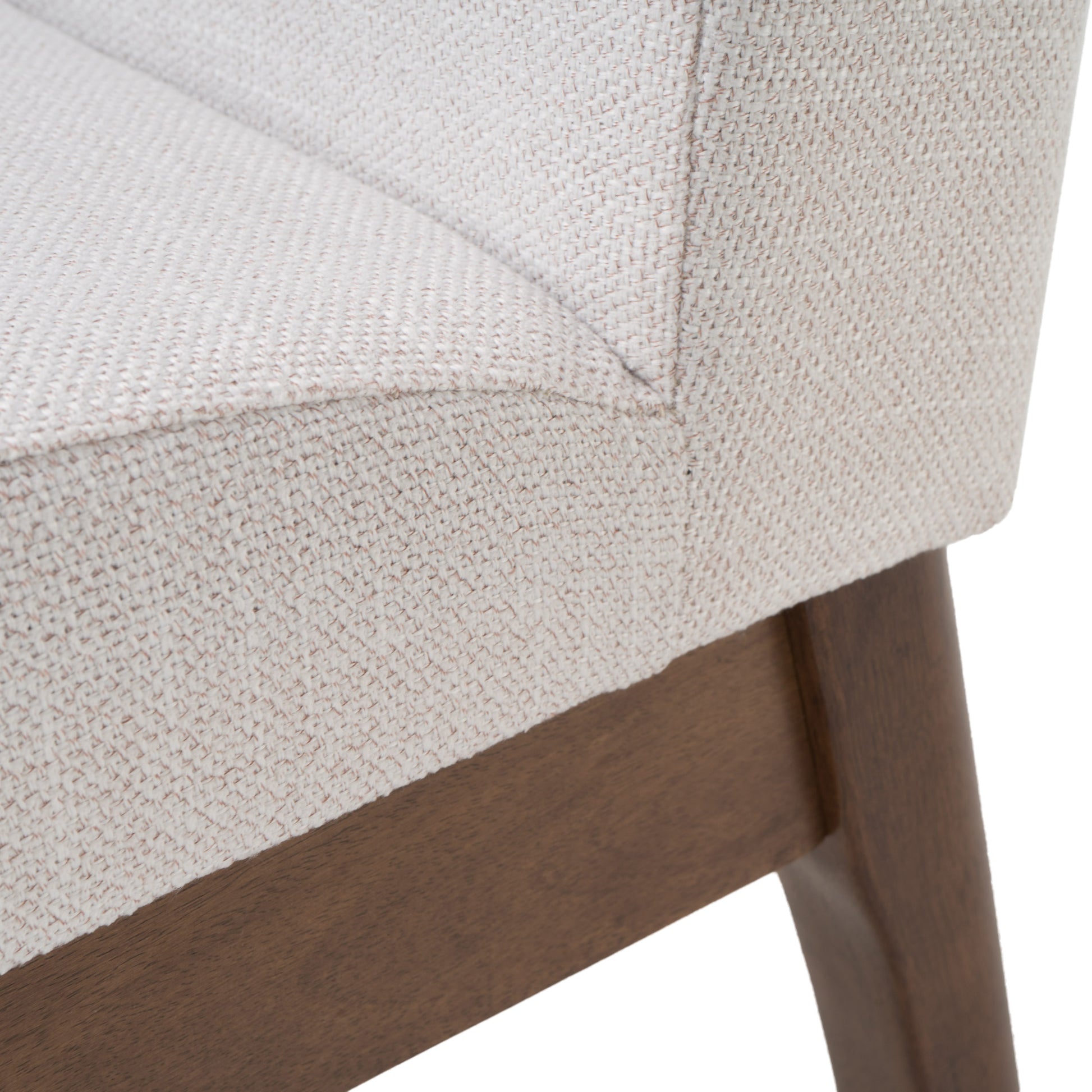 Closeup of textured light beige fabric on a chair seat with dark wood legs visible