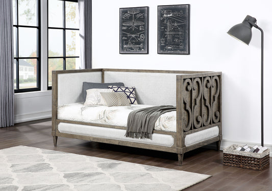 Rustic grey wood daybed with upholstered light grey fabric sides and decorative scrollwork