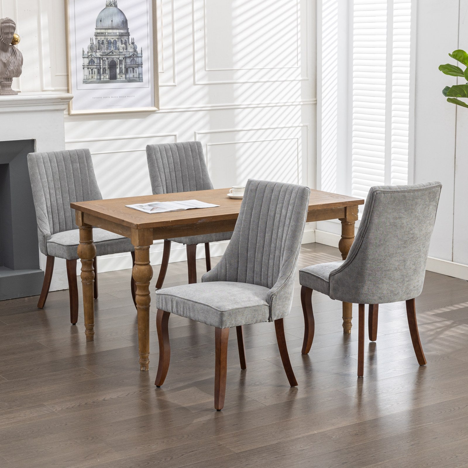 Four grey upholstered dining chairs with carved wooden legs around a rectangular wooden table