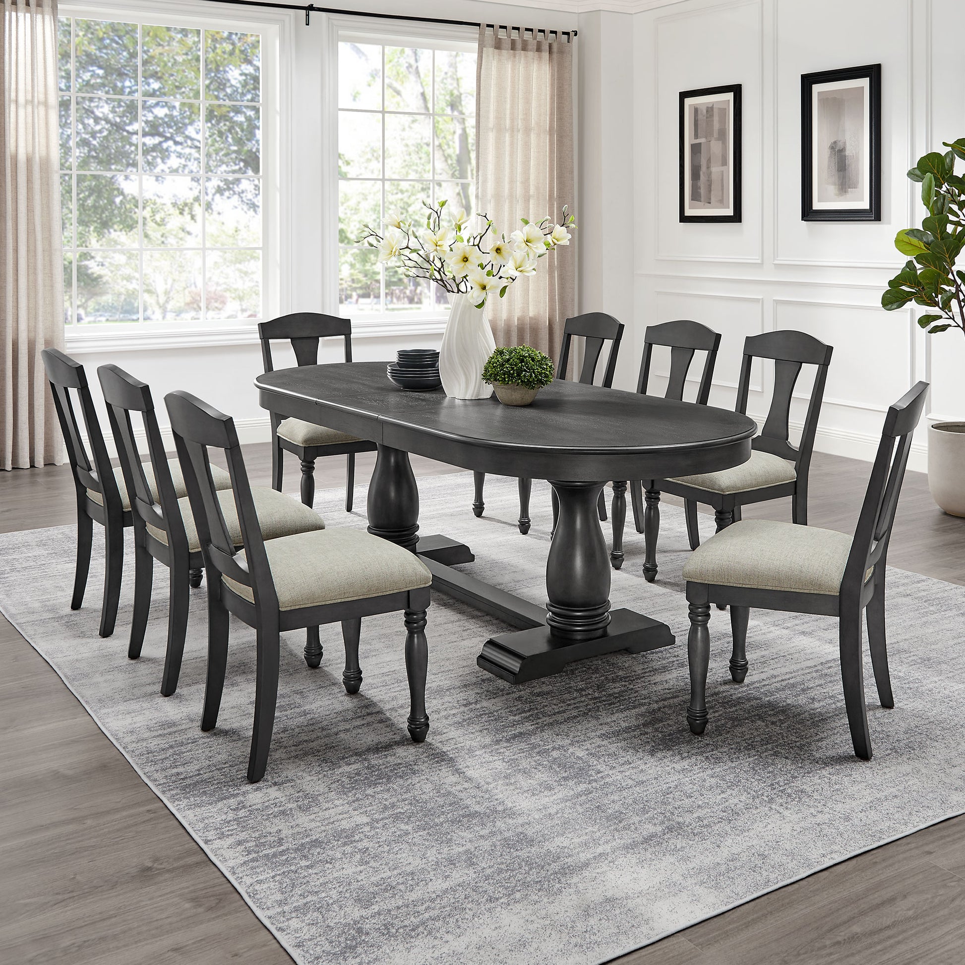Dark gray oval dining table with pedestal base and upholstered chairs