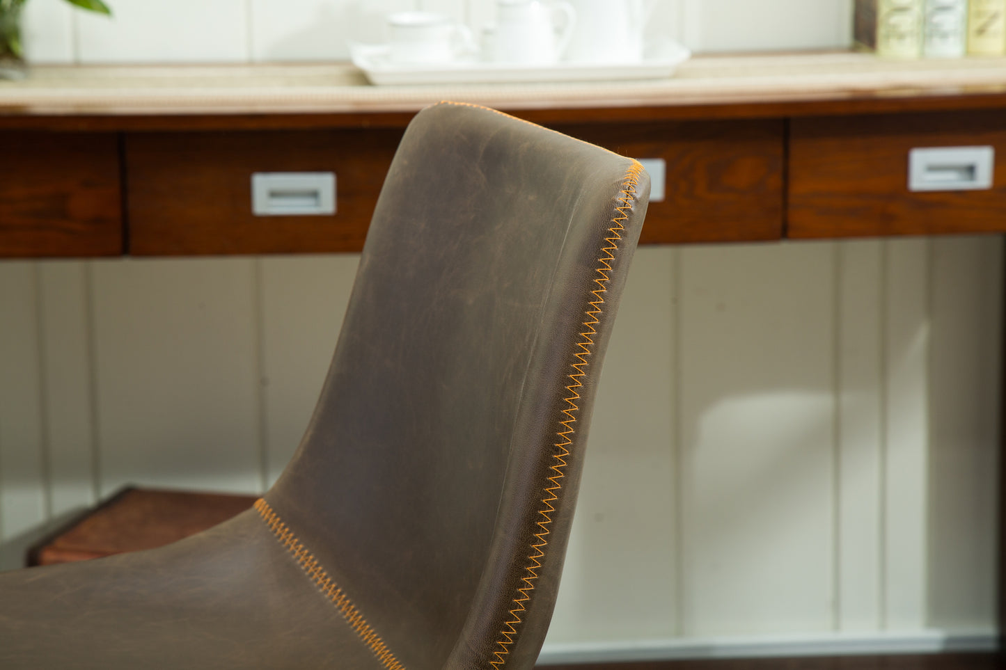 Brown leather dining chair with visible orange stitching along the seam