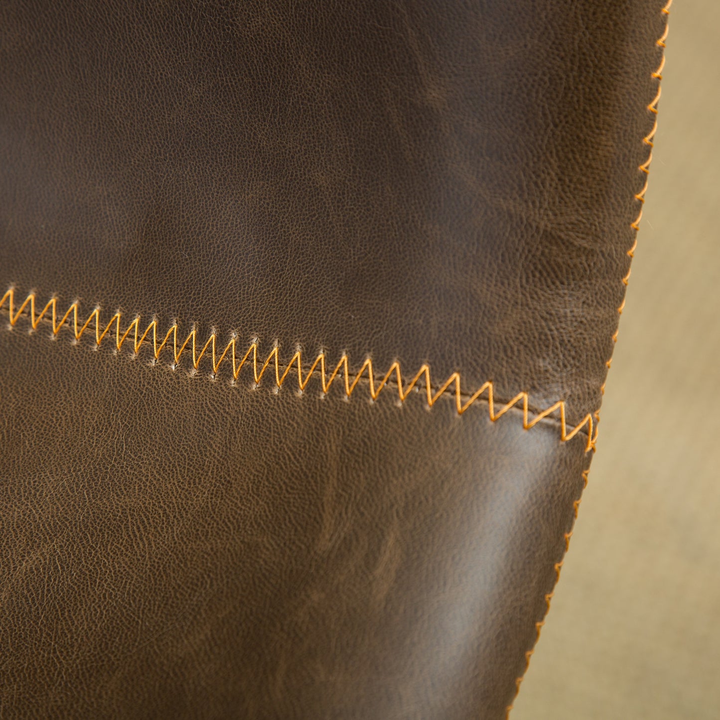 Closeup of dark brown leather with textured grain and thick orange stitching