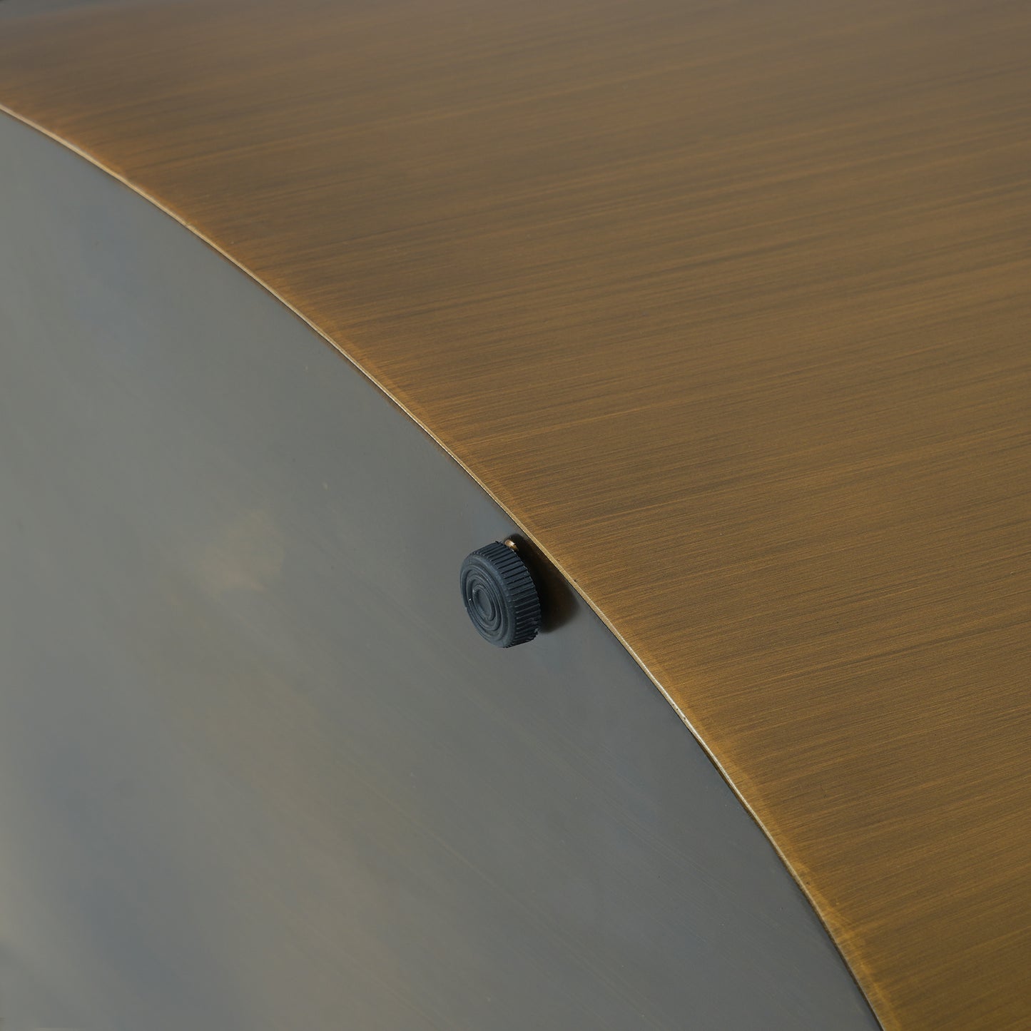 Closeup of brushed brass textured panel with dark gray accent and black knob