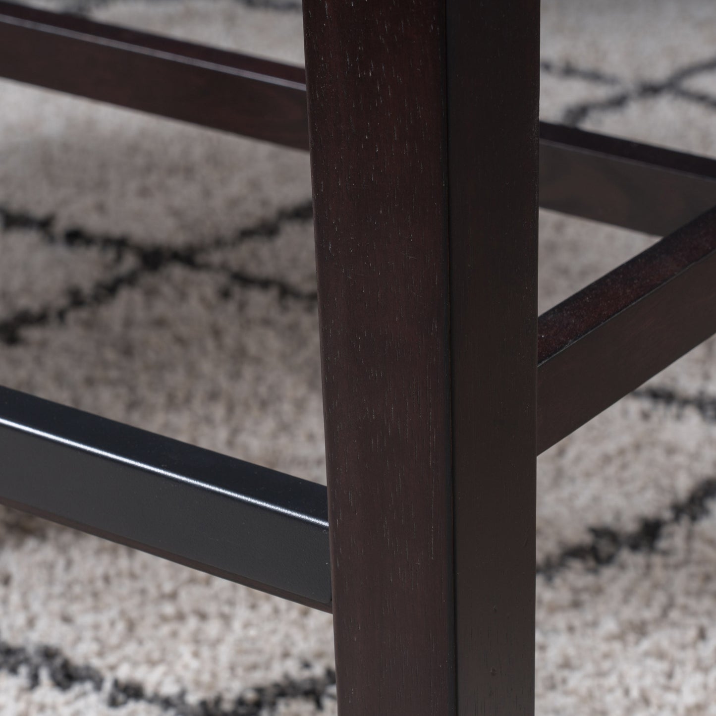 Dark mahogany wood bar stool leg detail on textured rug