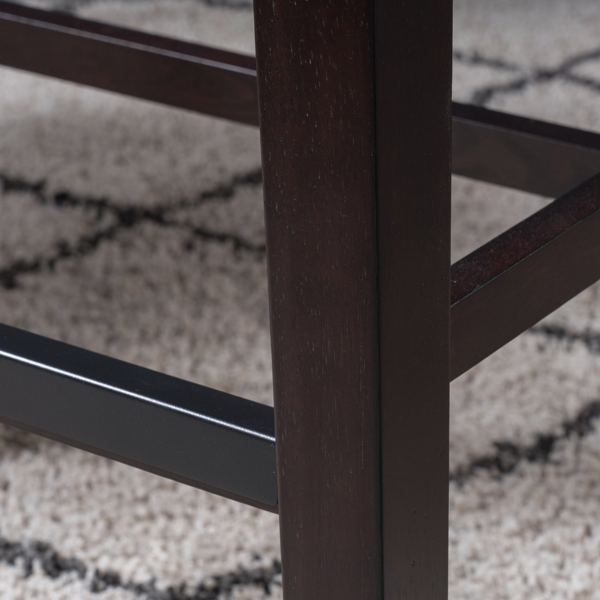 Dark mahogany wood bar stool leg detail on textured rug