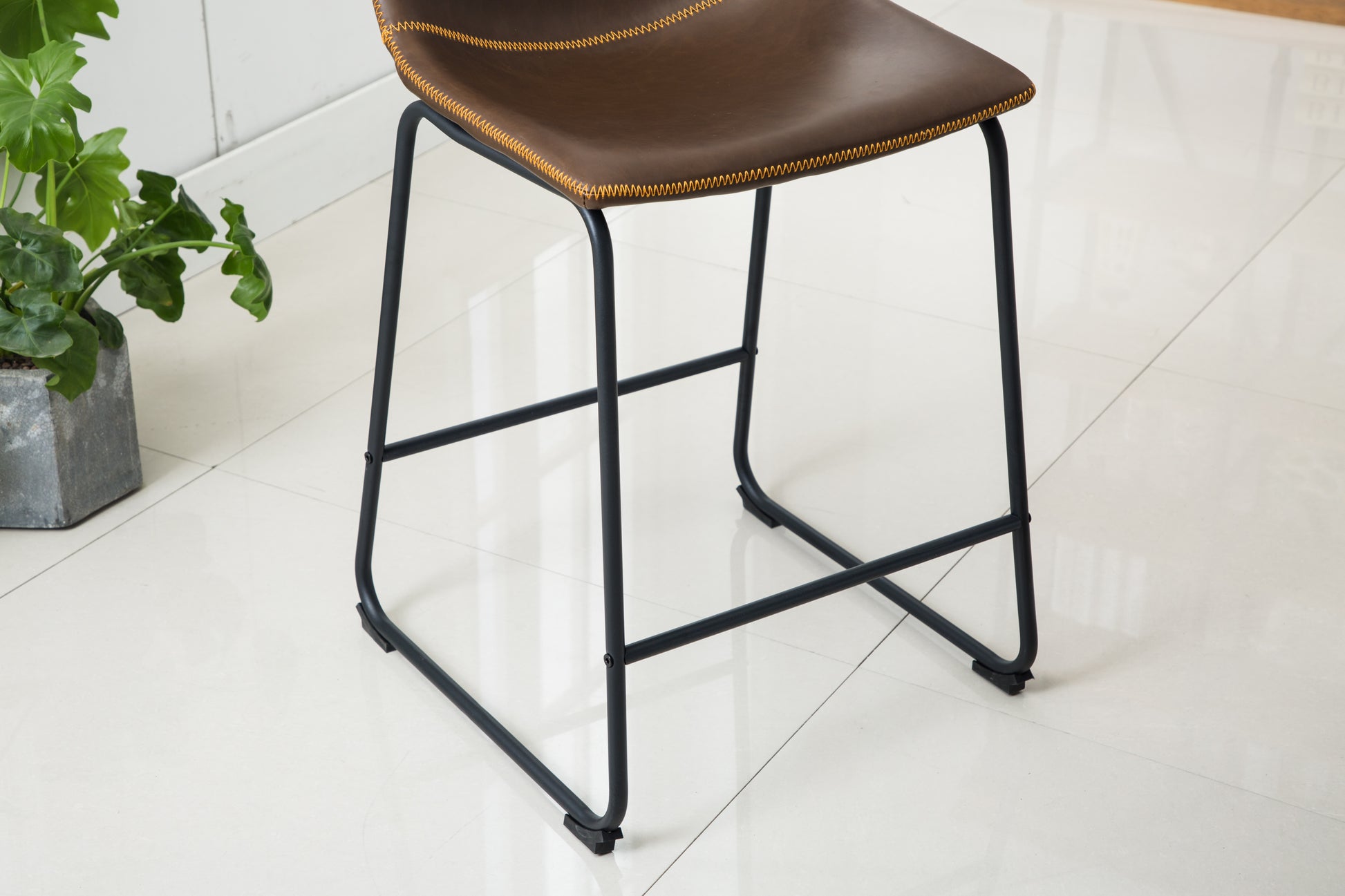 Brown leather bar stool with orange stitching and black metal legs