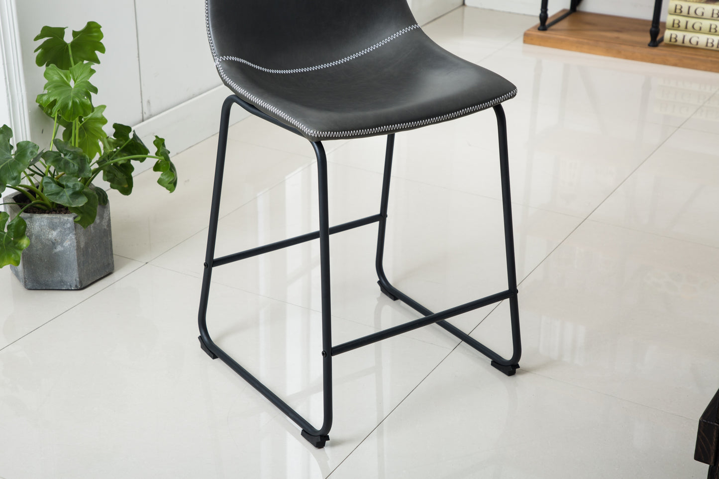 Black faux leather counter stool with white stitching and slim metal legs