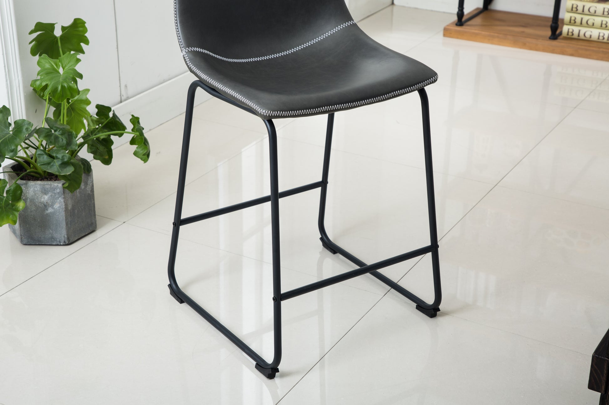 Black faux leather counter stool with white stitching and slim metal legs