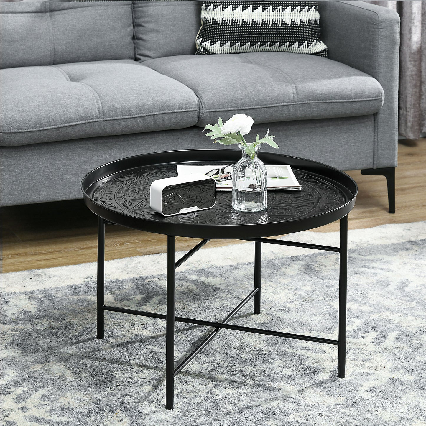 Black metal round coffee table with embossed pattern featuring a white clock and vase