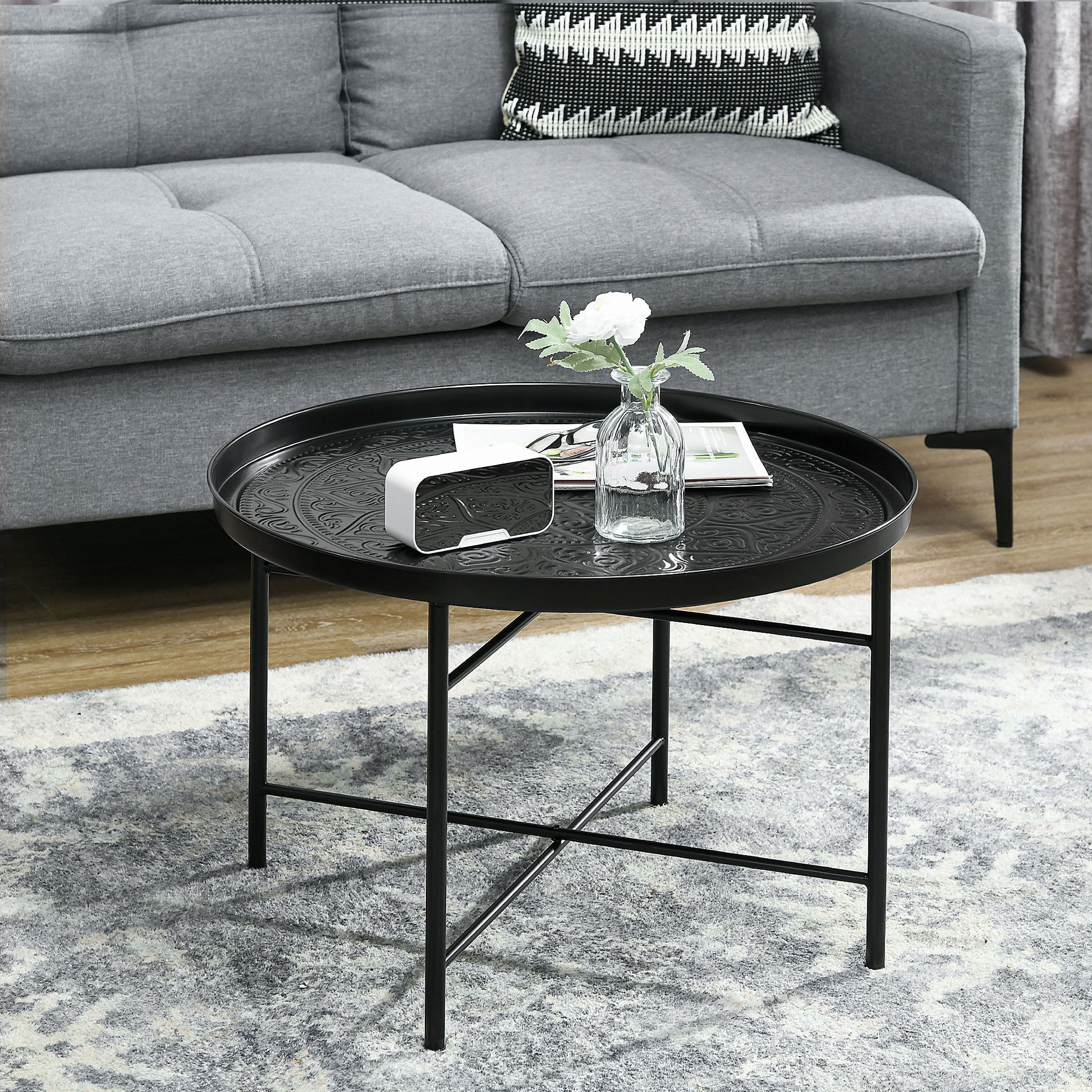 Black metal round coffee table with embossed pattern featuring a white clock and vase