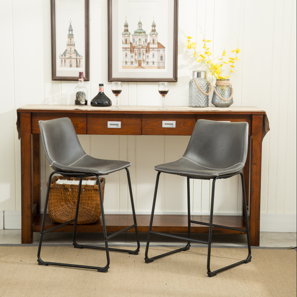Two dark gray faux leather bar stools with white stitching and black metal legs