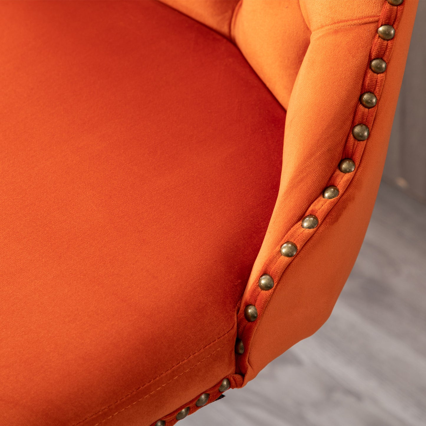 Closeup of an orange velvet armchair with antique brass nailhead trim