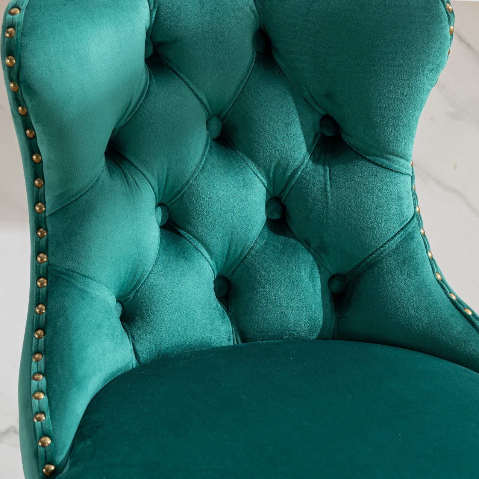 Deep emerald velvet dining chair with button tufting and gold nailhead trim