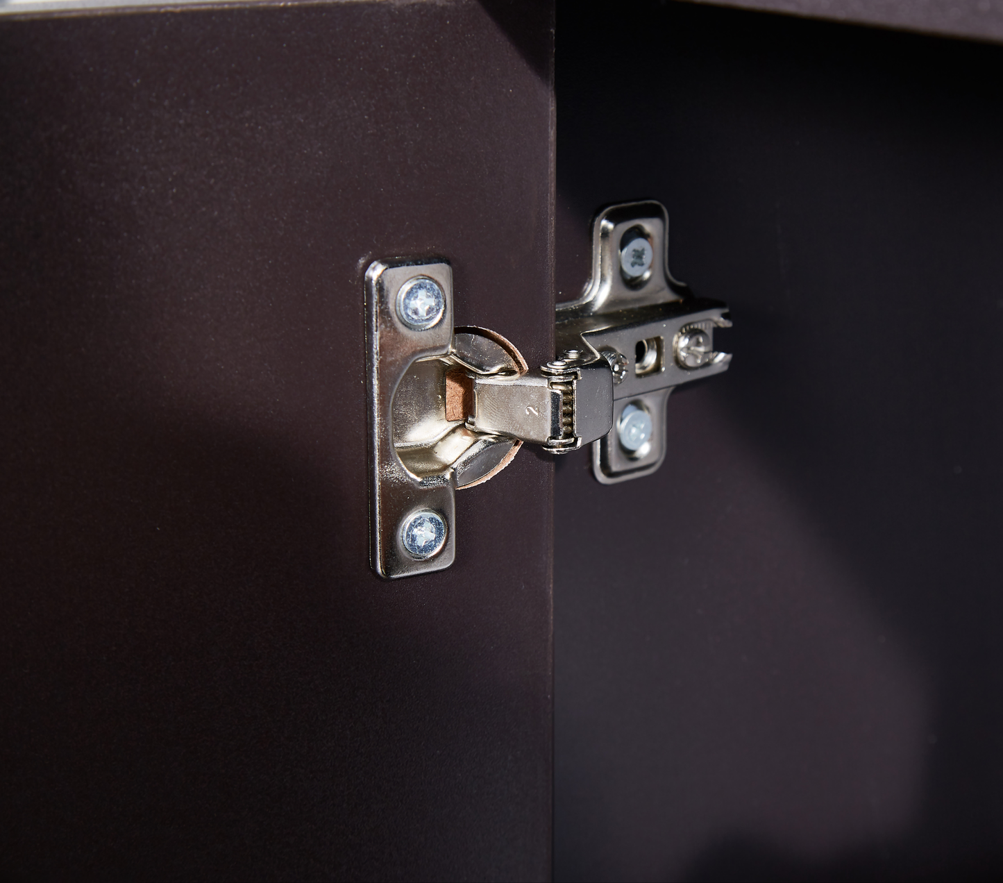 Closeup of a metal cabinet hinge mechanism on a dark brown door panel