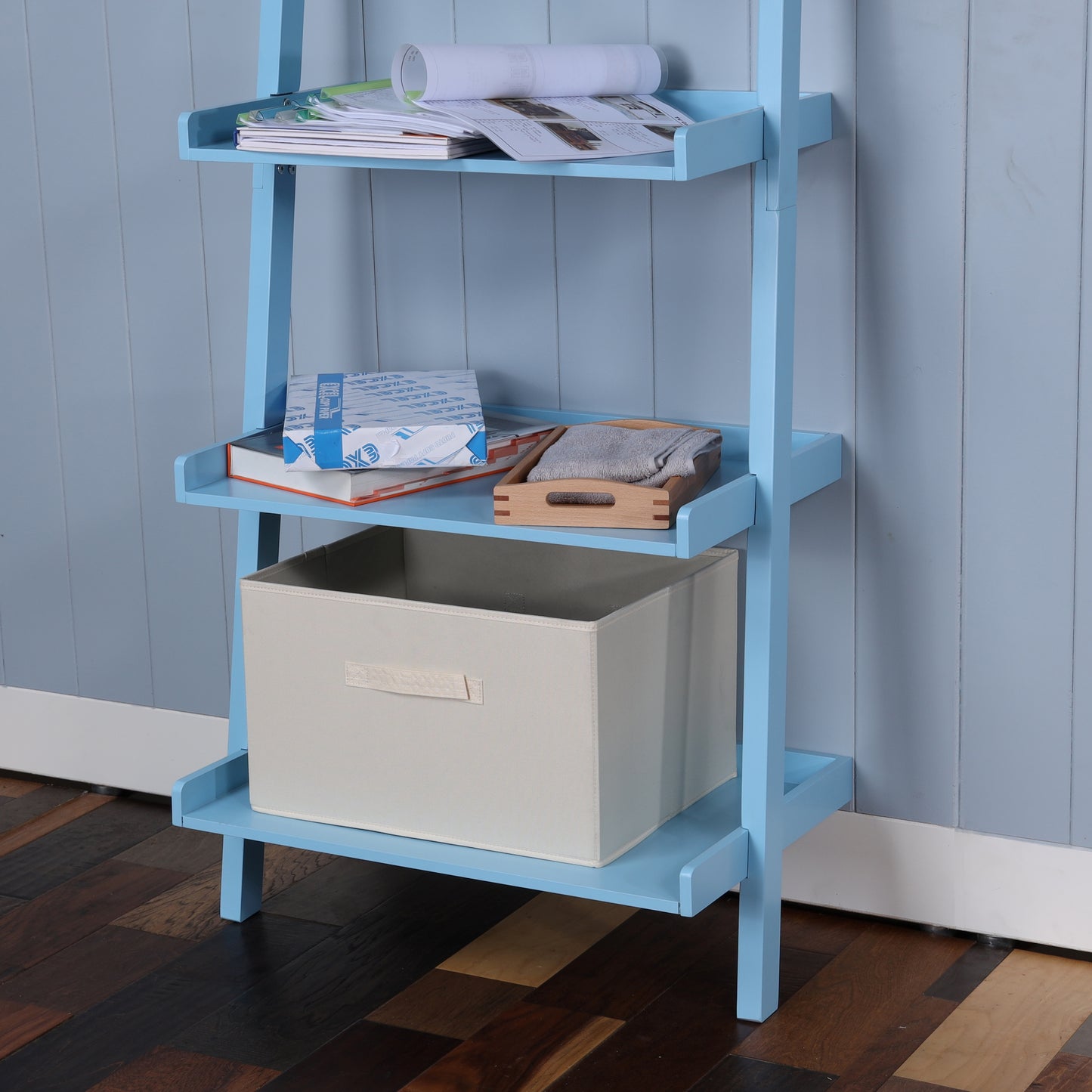 Light blue ladder bookshelf with stacked books and storage bin