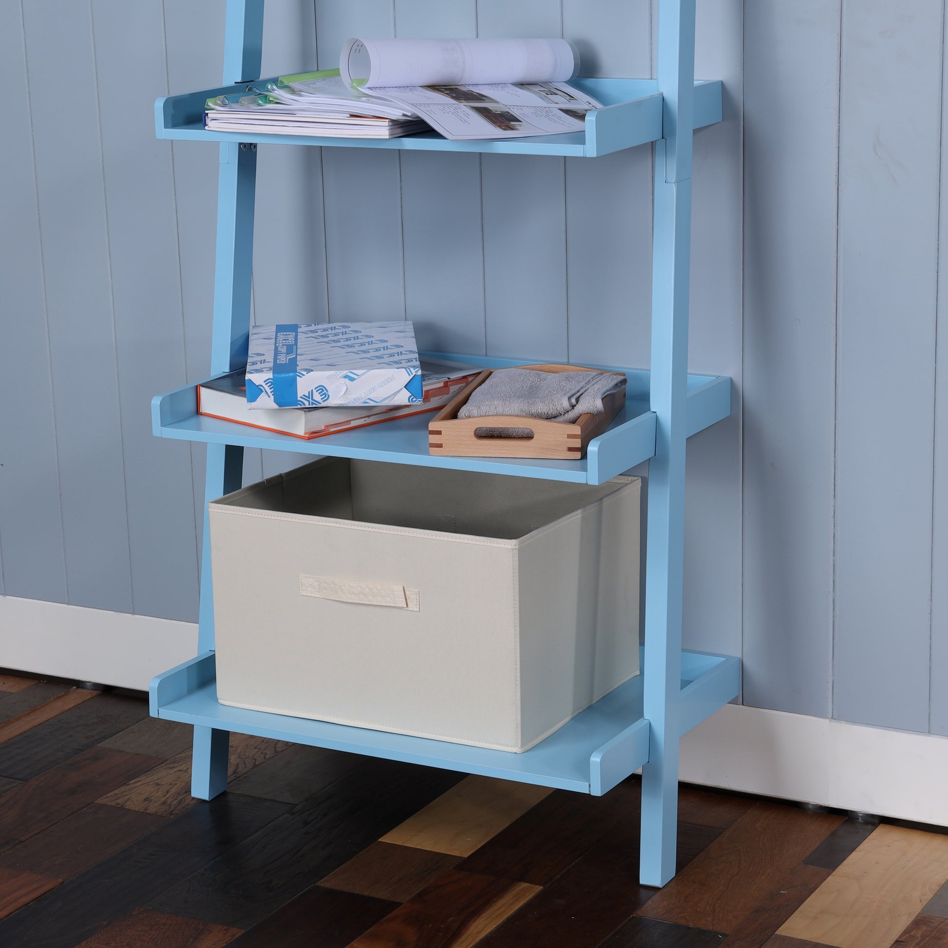 Light blue ladder bookshelf with stacked books and storage bin