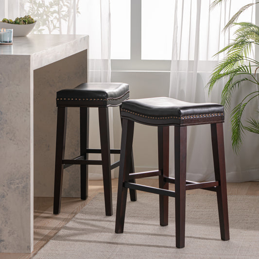 Two black faux leather bar stools with nailhead trim and dark wood legs