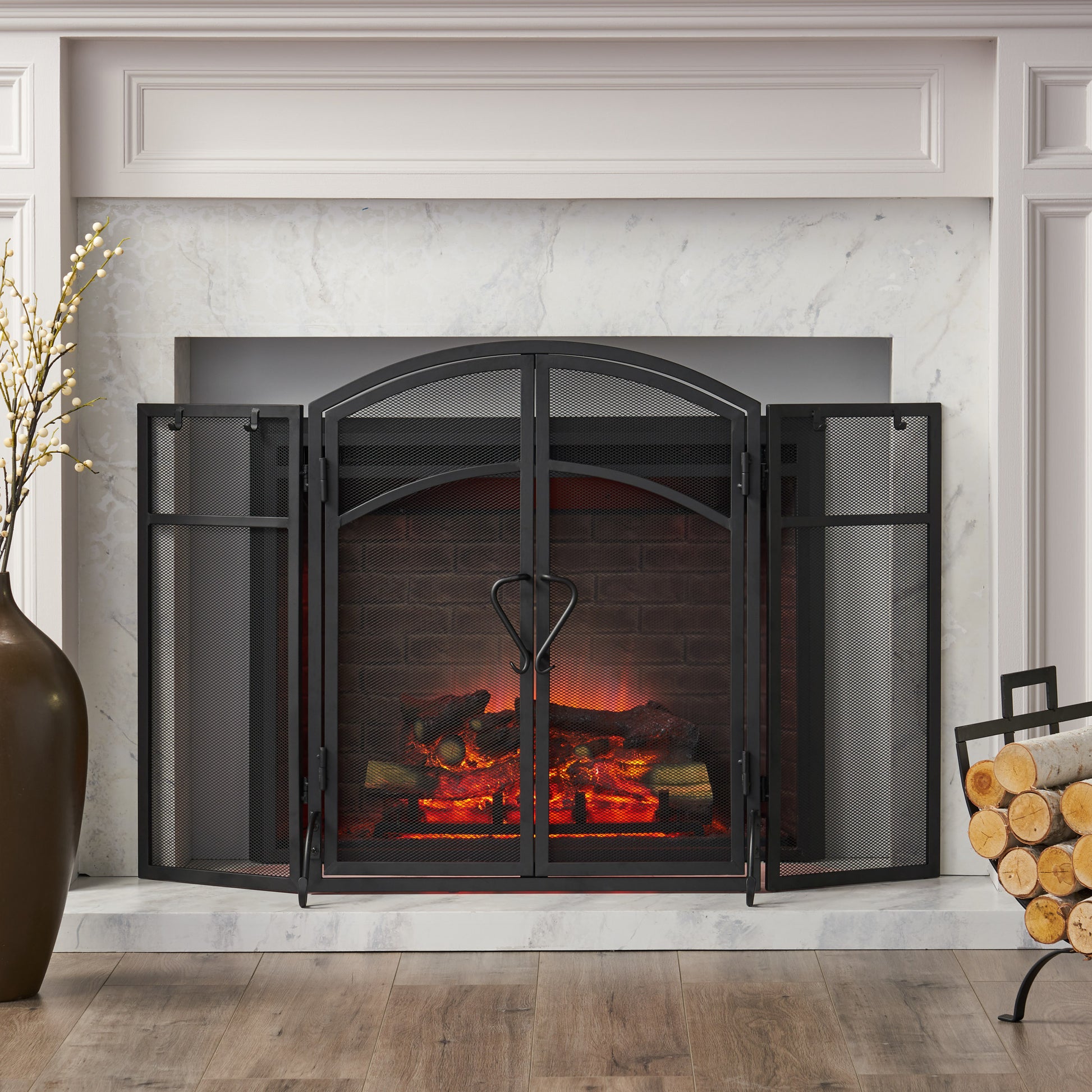 Black arched metal fireplace screen with  folding panels guarding a brick fireplace with logs