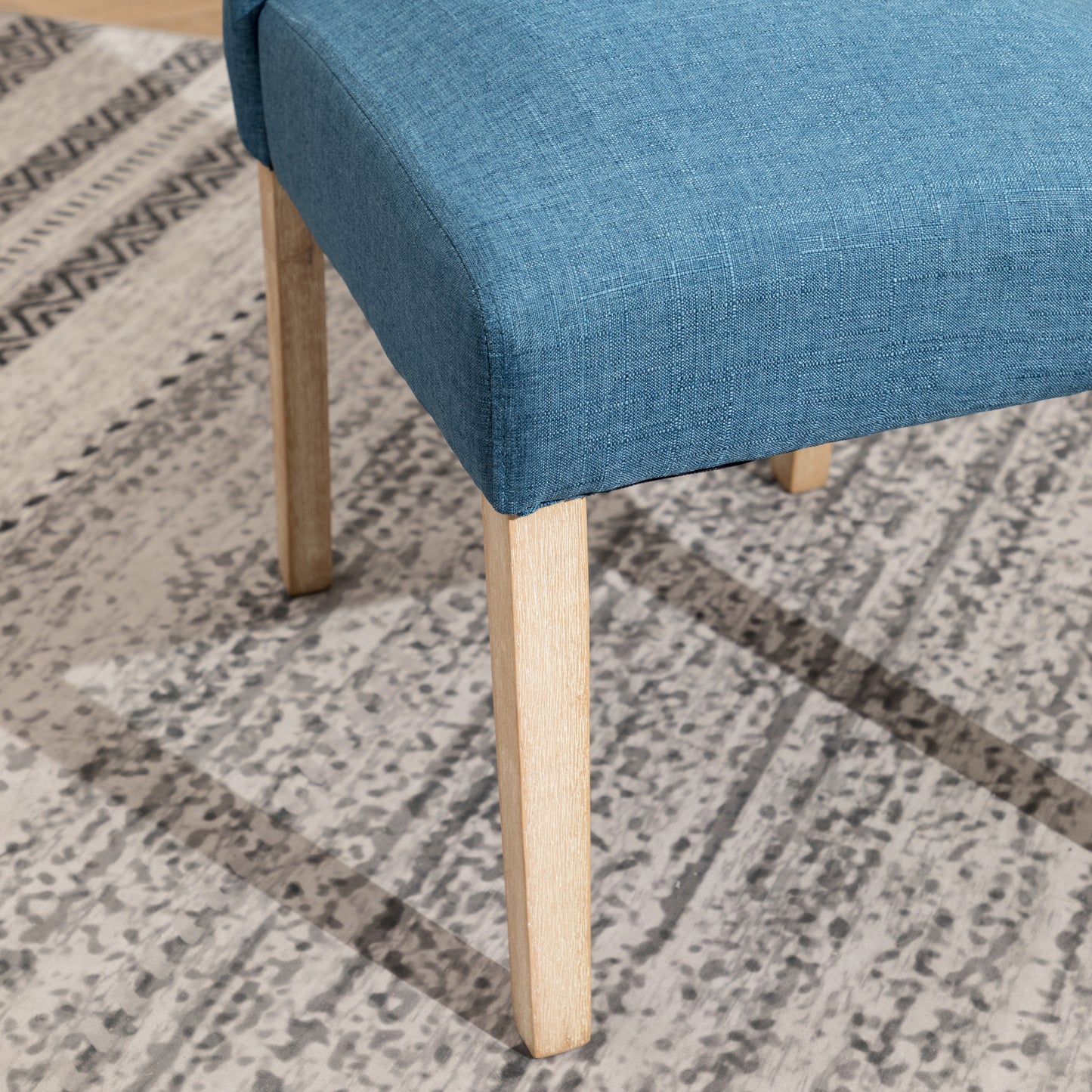 Blue fabric dining chair seat with light wood legs on patterned rug