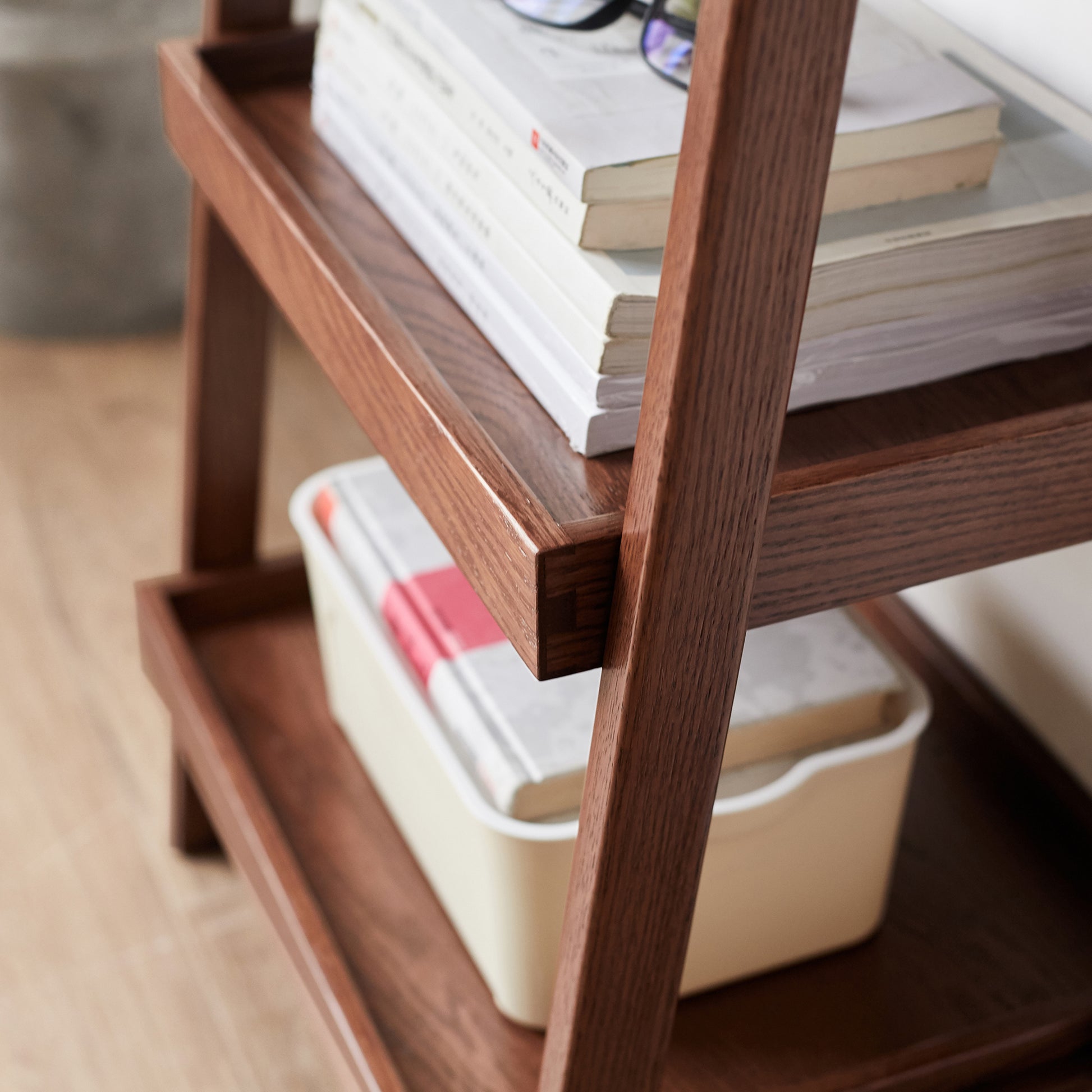Dark oak ladder shelf with stacked books and storage bin