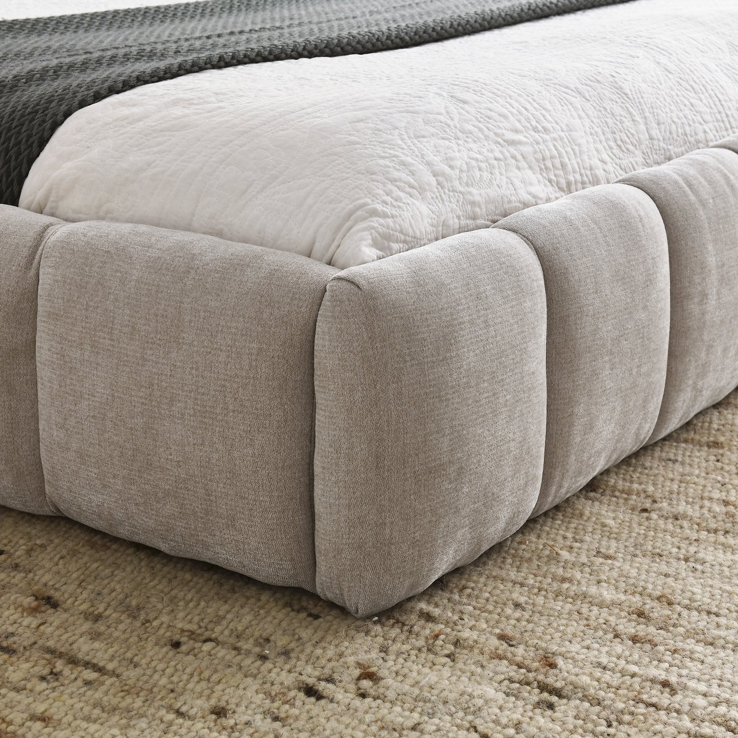 Modern upholstered bed frame in neutral beige fabric with a quilted white mattress and charcoal throw blanket