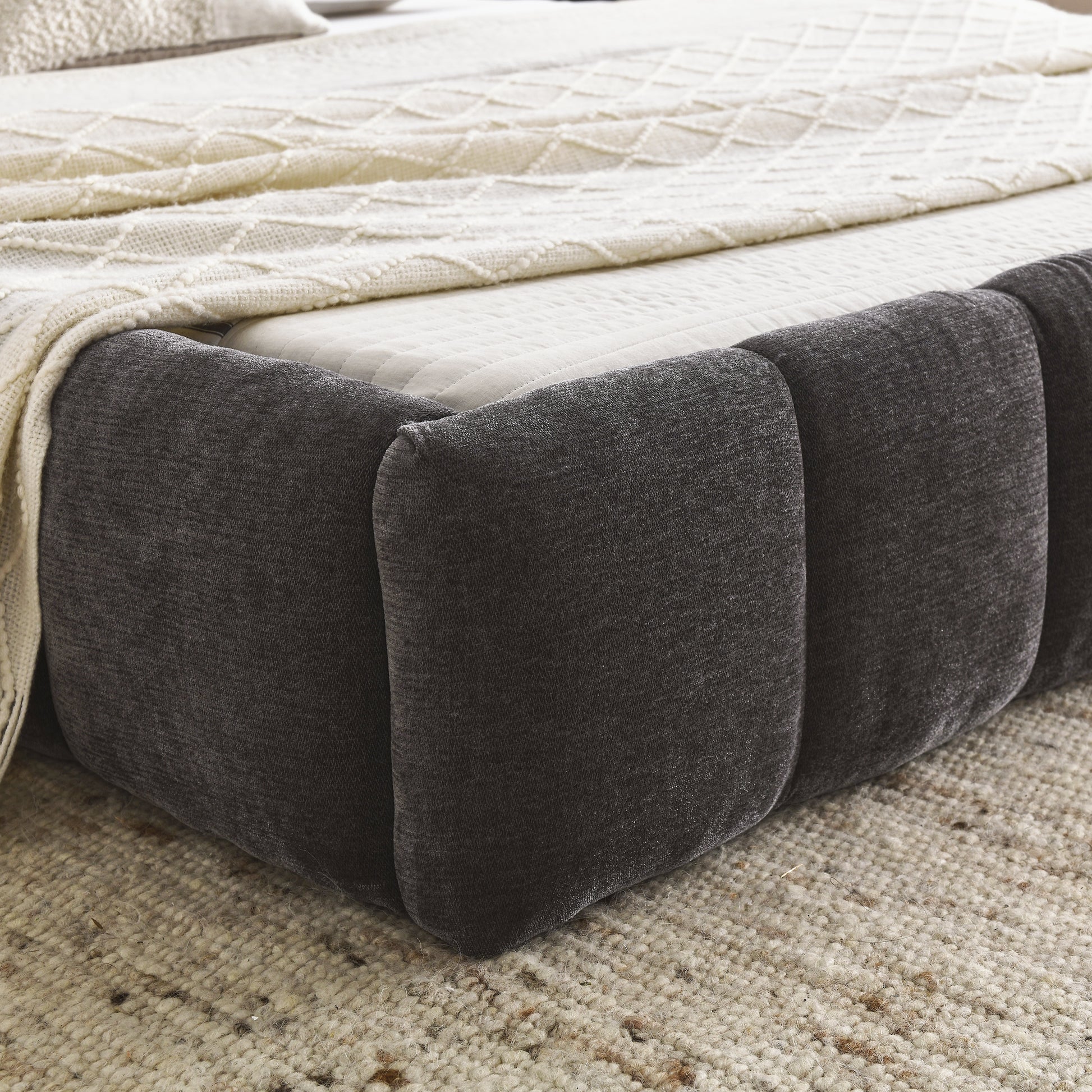 Dark grey upholstered bed frame with quilted mattress and cream knit throw
