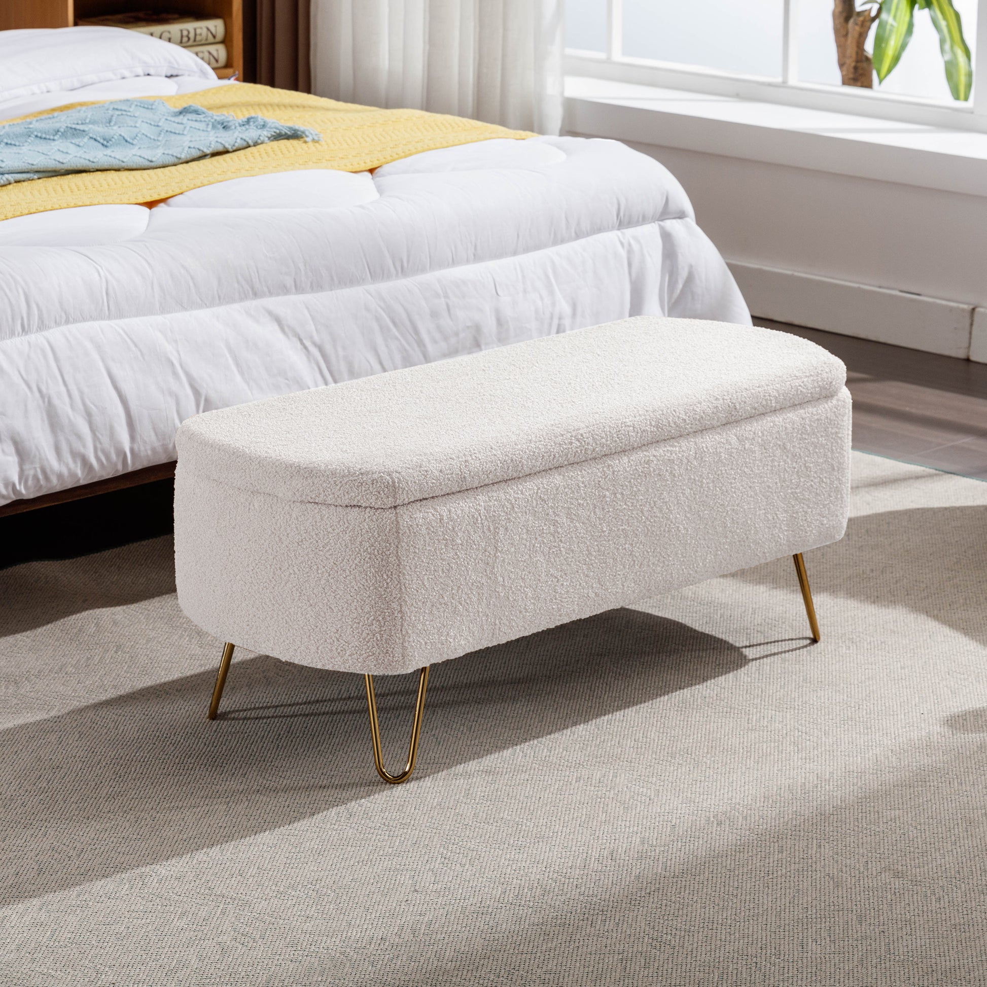 Cream boucle storage bench with gold hairpin legs at foot of bed