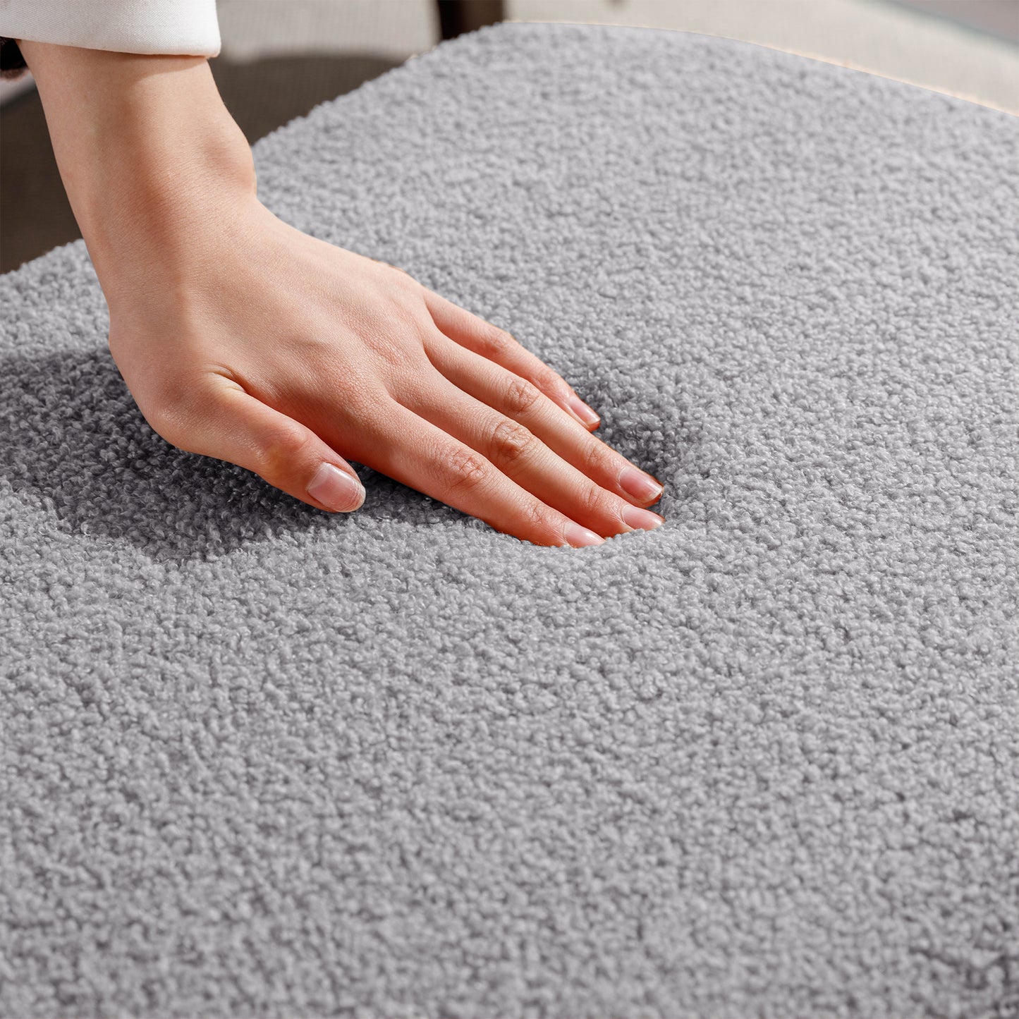Closeup of a hand pressing into soft grey boucle fabric chair seat showcasing plush comfort