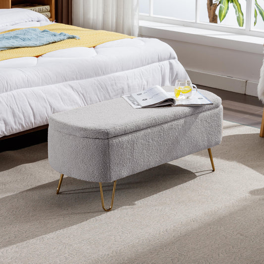 Grey teddy fabric storage ottoman with gold legs beside a bed