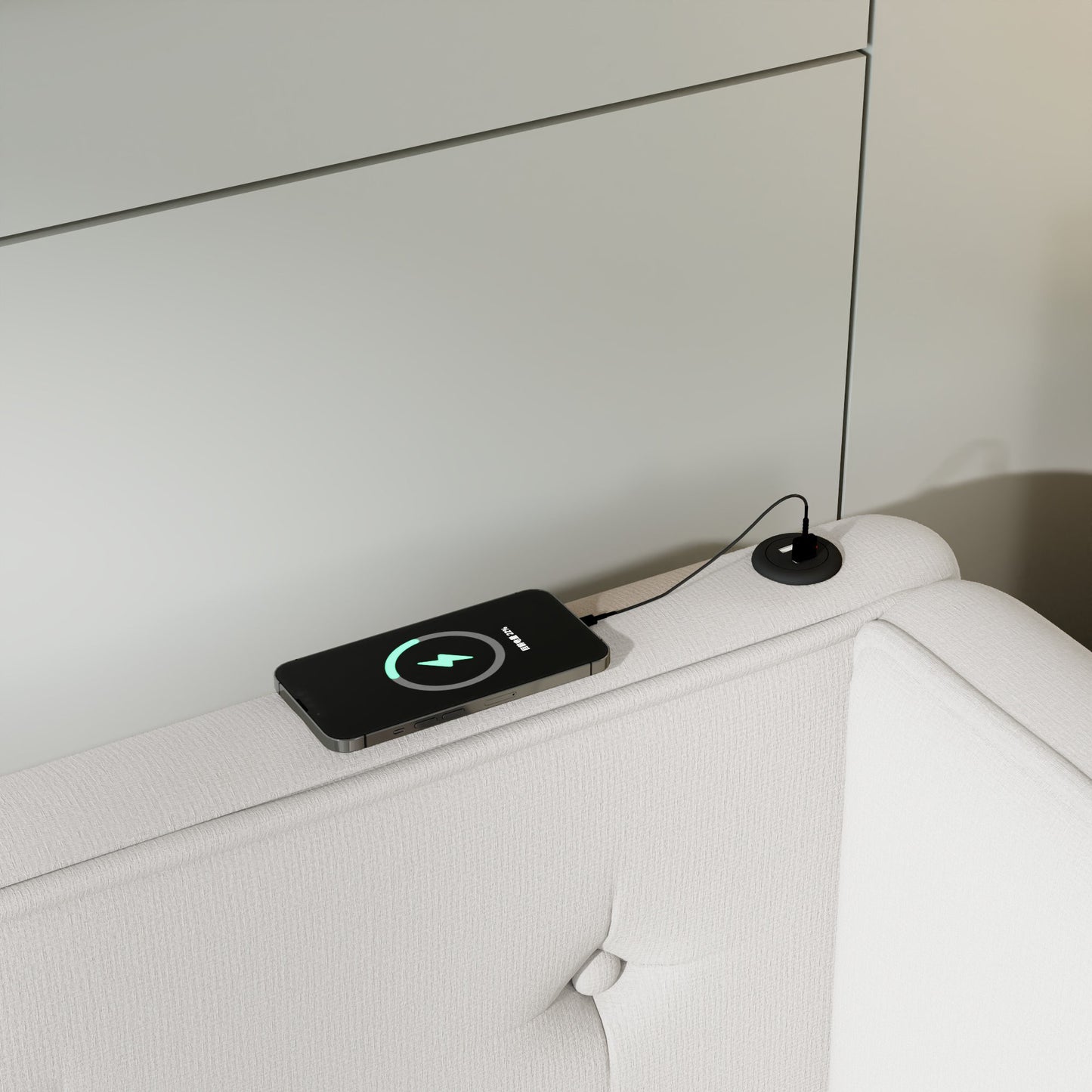 Black smartphone wirelessly charging on a white upholstered furniture armrest