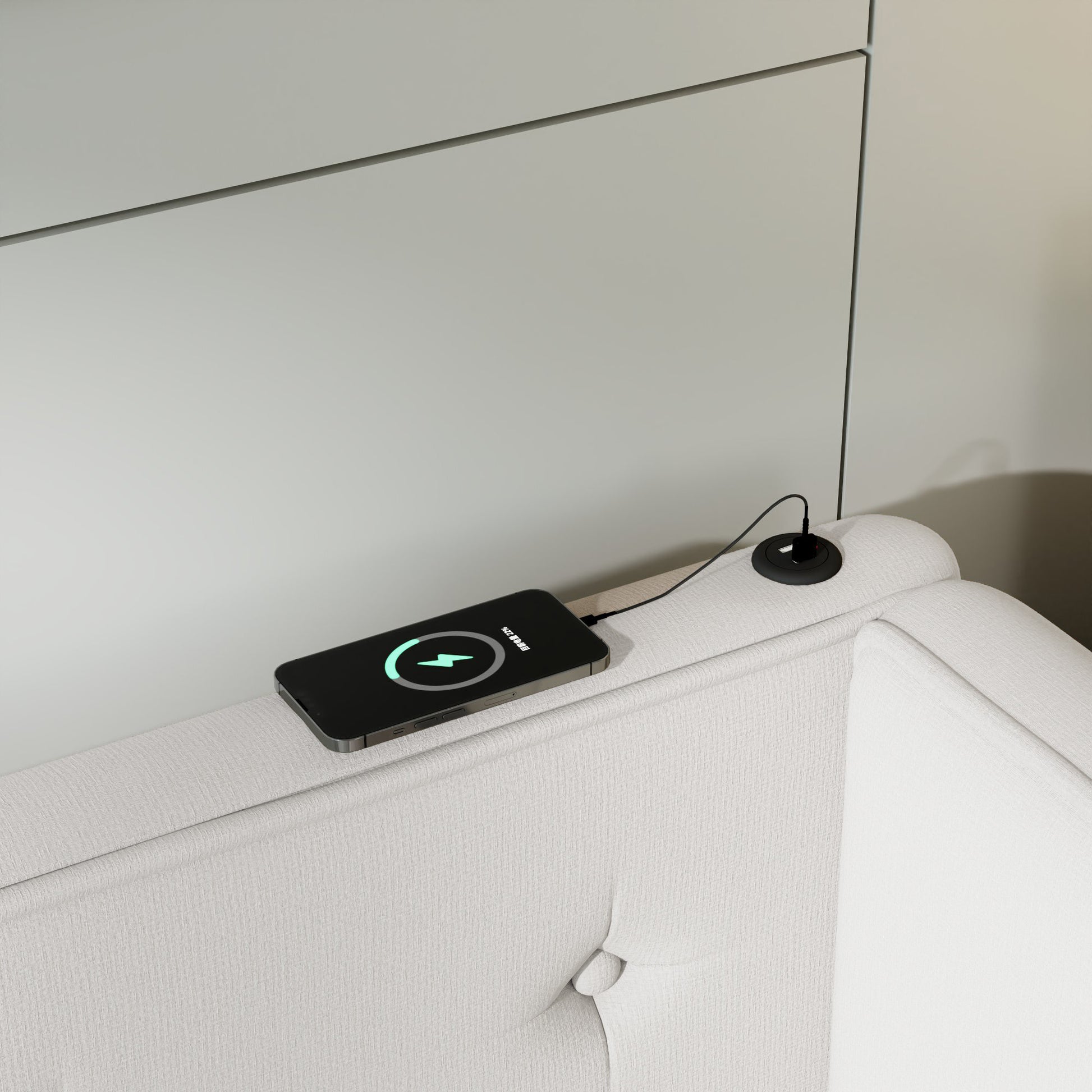 Black smartphone wirelessly charging on a white upholstered furniture armrest