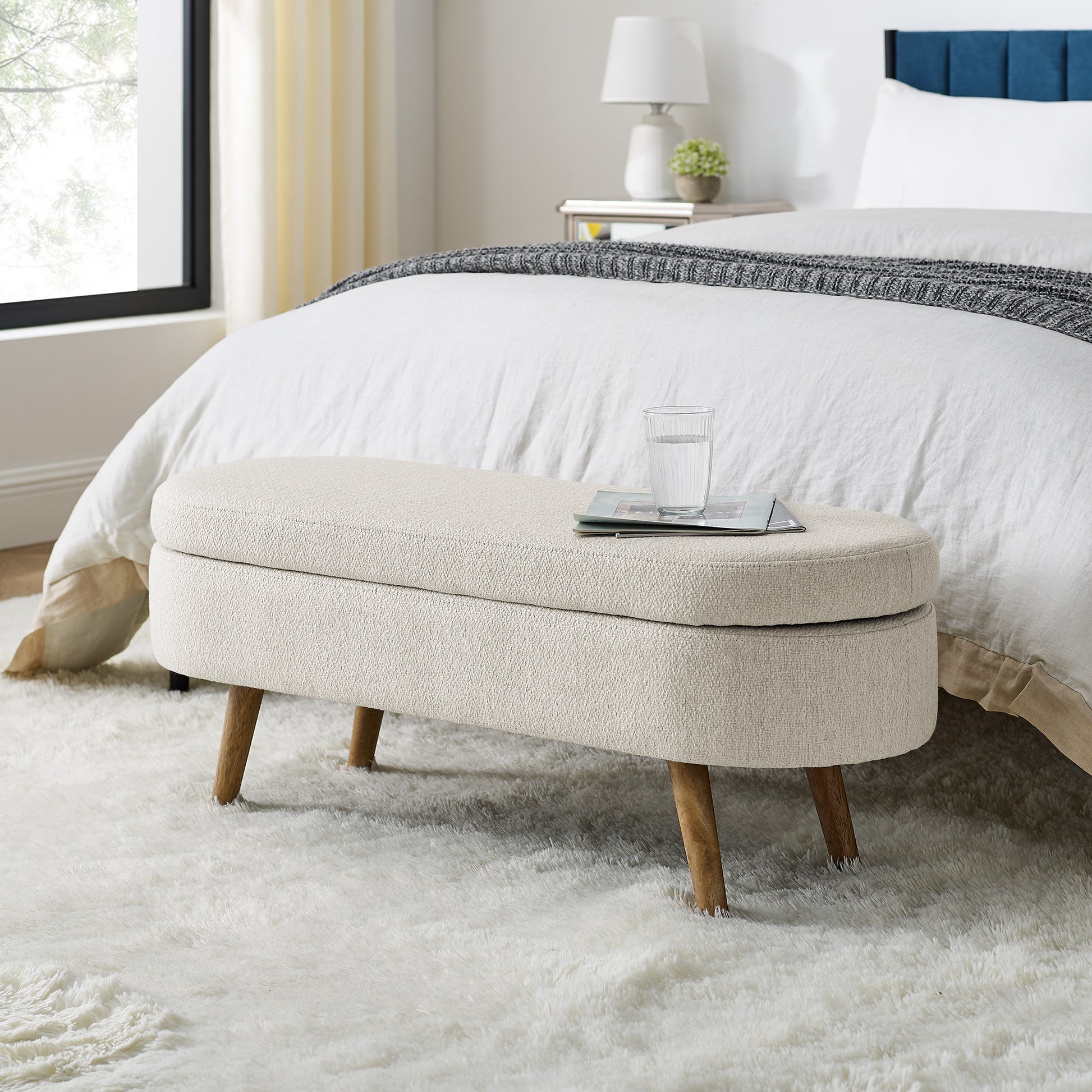 Cream boucle storage ottoman with wooden legs at foot of bed